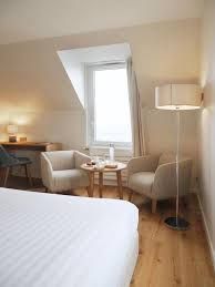 Chambre d’hôtel confortable avec lit, bureau, fauteuils, lampadaire et fenêtre lumineuse