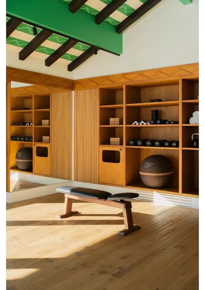 Studio de yoga lumineux avec des étagères en bois, un banc et des poutres vertes au plafond