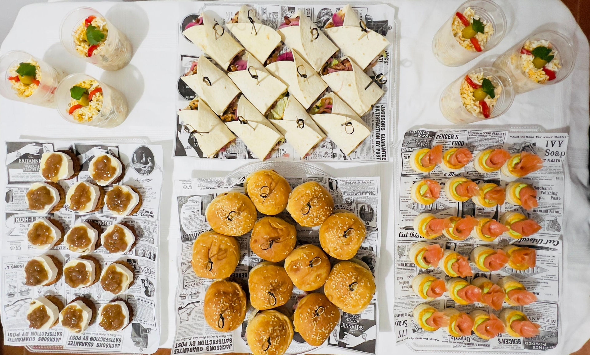 Variedad de aperitivos y postres presentados en bandejas, que incluyen sándwiches, pasteles y bocaditos decorados.