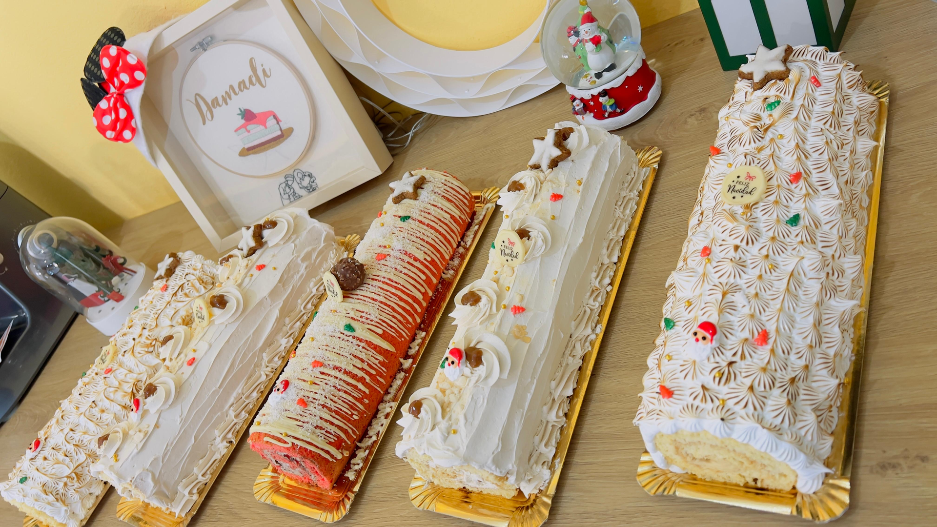 Variedad de rollos suizos decorados sobre una mesa, cubiertos con crema batida y detalles en rojo.