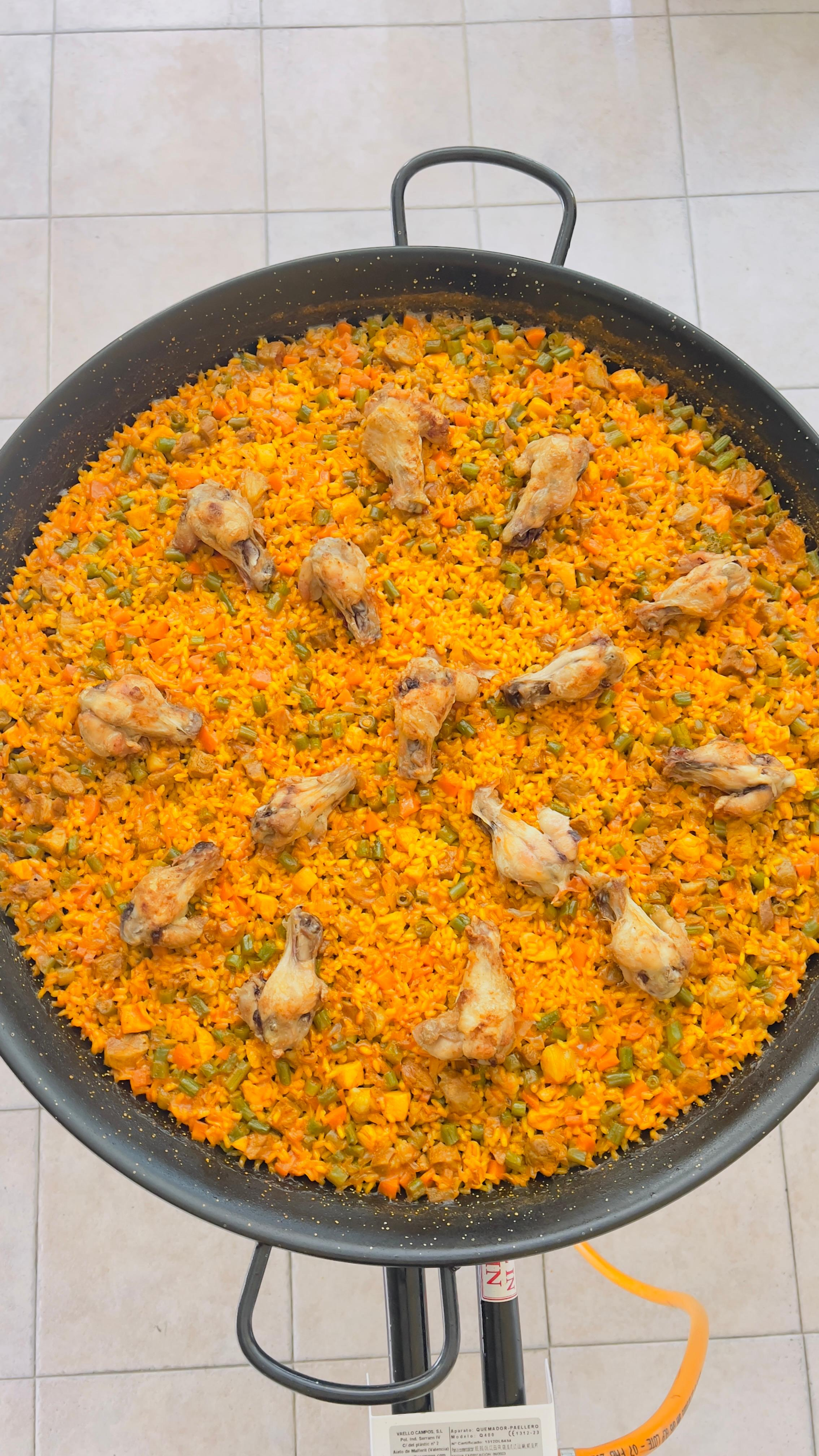 Gran olla de arroz naranja con trozos de carne, vista desde arriba sobre una estufa.