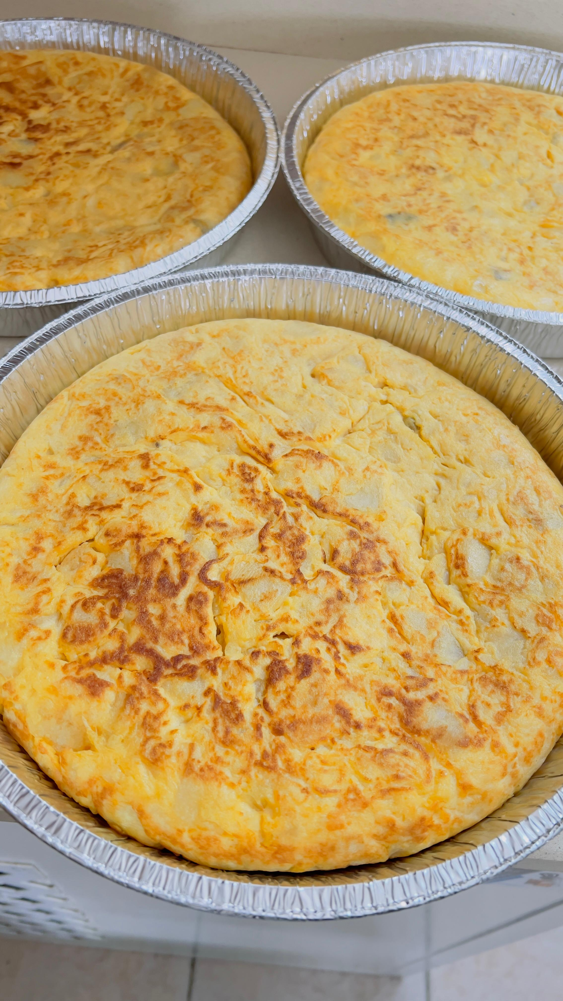 Tres cazuelas de queso horneadas en bandejas desechables de aluminio, doradas por encima.