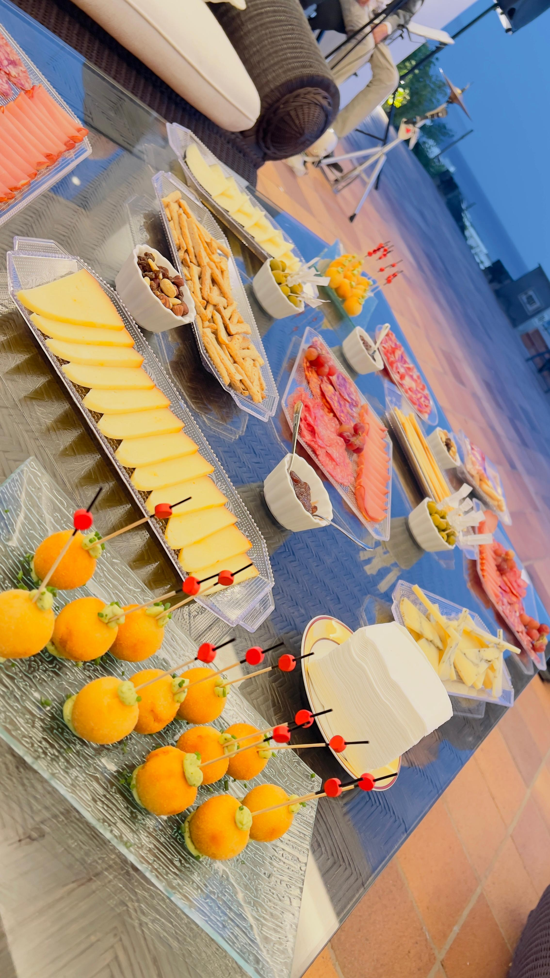 Bufé de postres con pasteles variados y brochetas de fruta sobre una mesa de azulejos al aire libre.