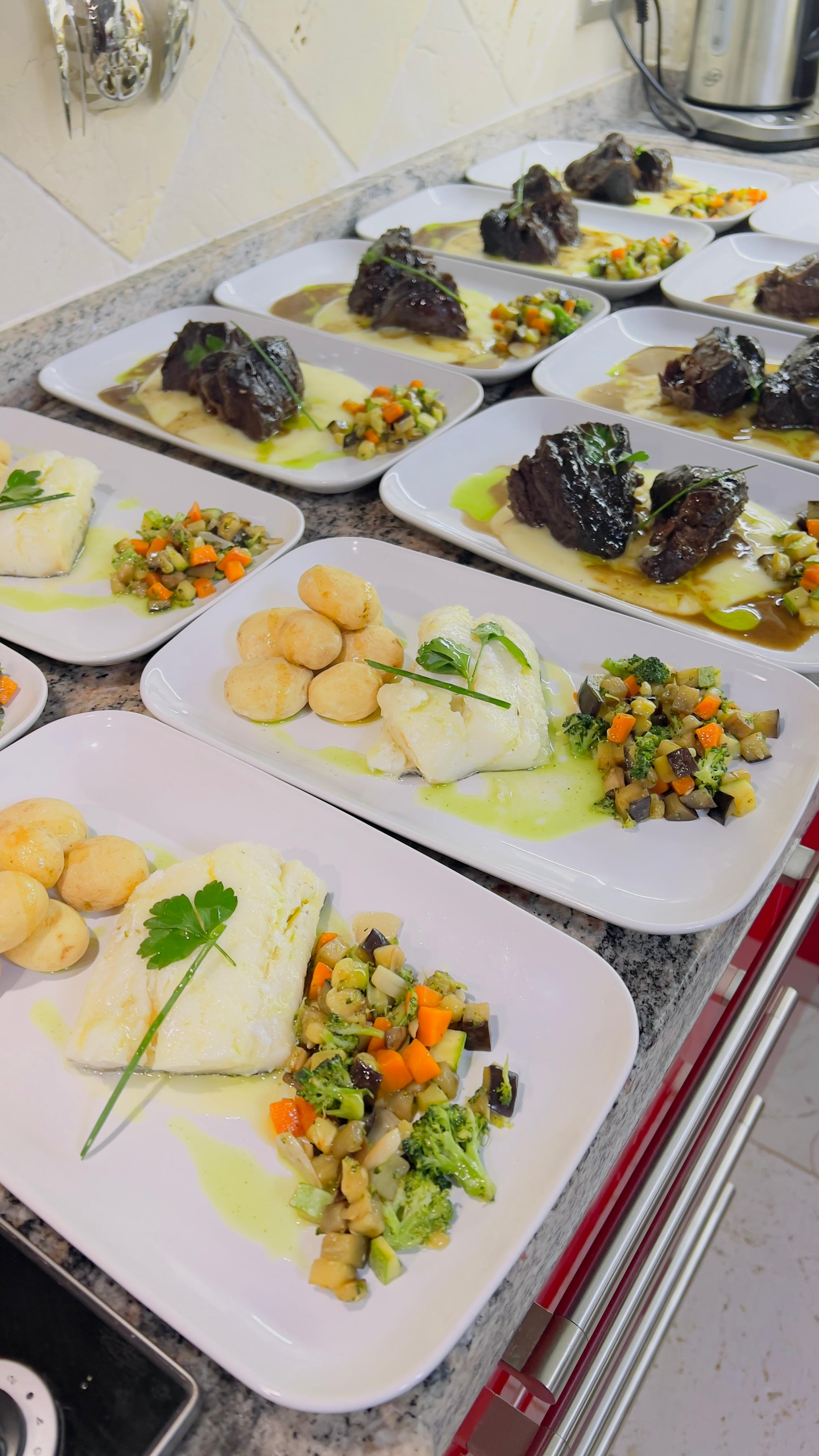 Platos gourmet de pescado emplatados, acompañados de verduras y salsas, dispuestos sobre una encimera de cocina.