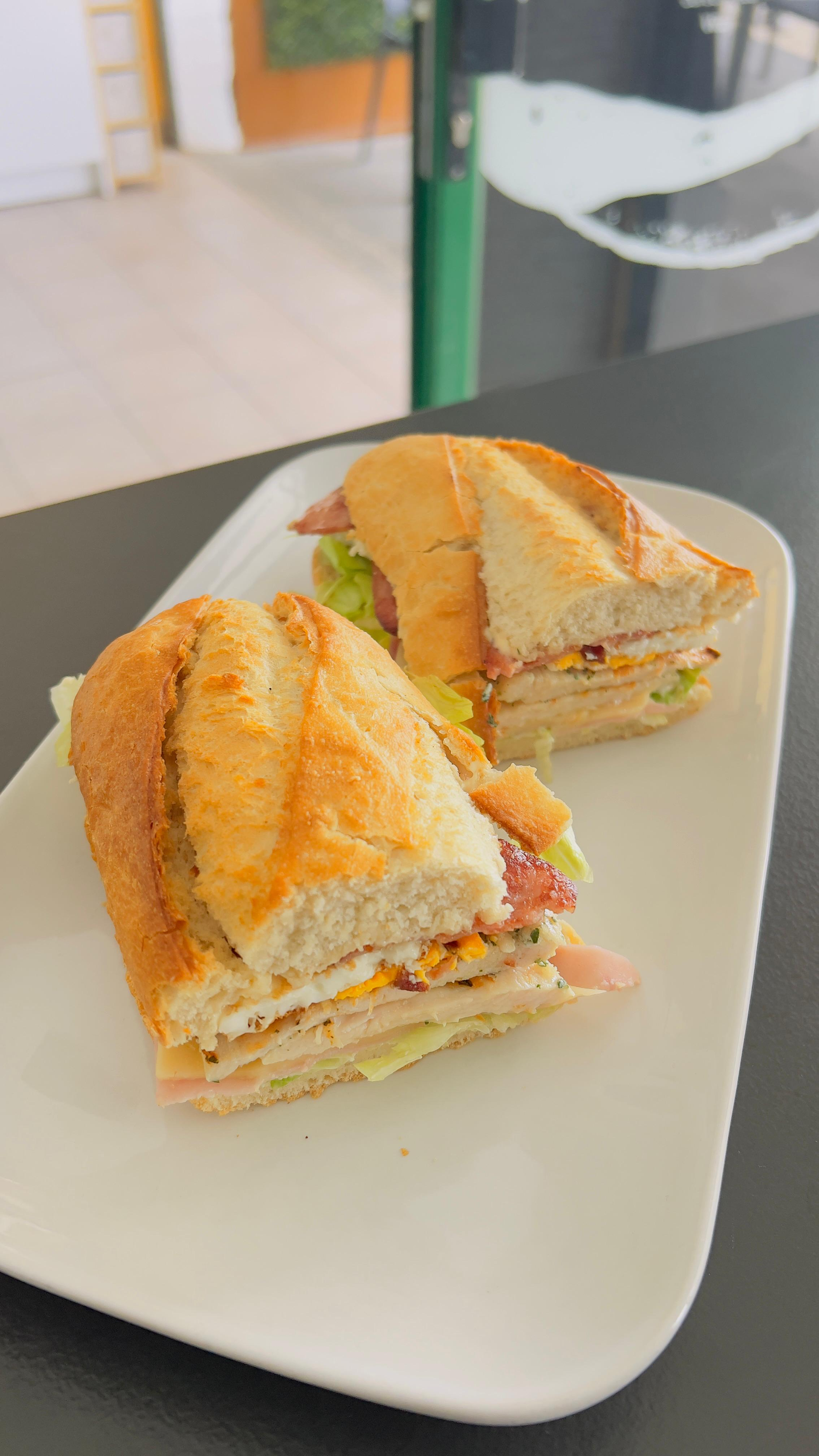 Dos sándwiches en un plato blanco, cortados por la mitad, con relleno de naranja sobre una mesa.