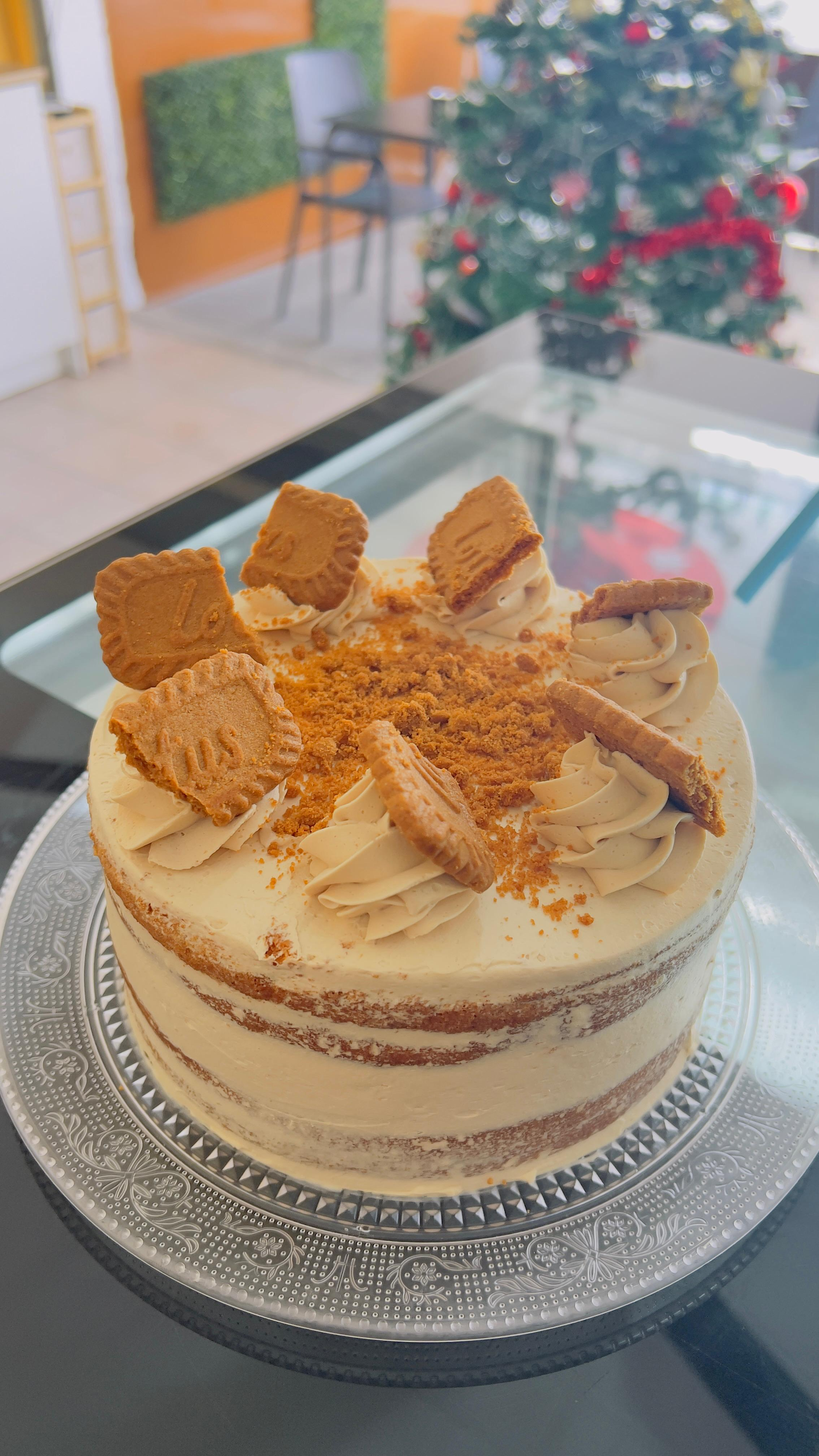 Tarta de crema en capas cubierta con virutas de caramelo sobre una mesa de cristal, con un árbol de Navidad borroso al fondo.