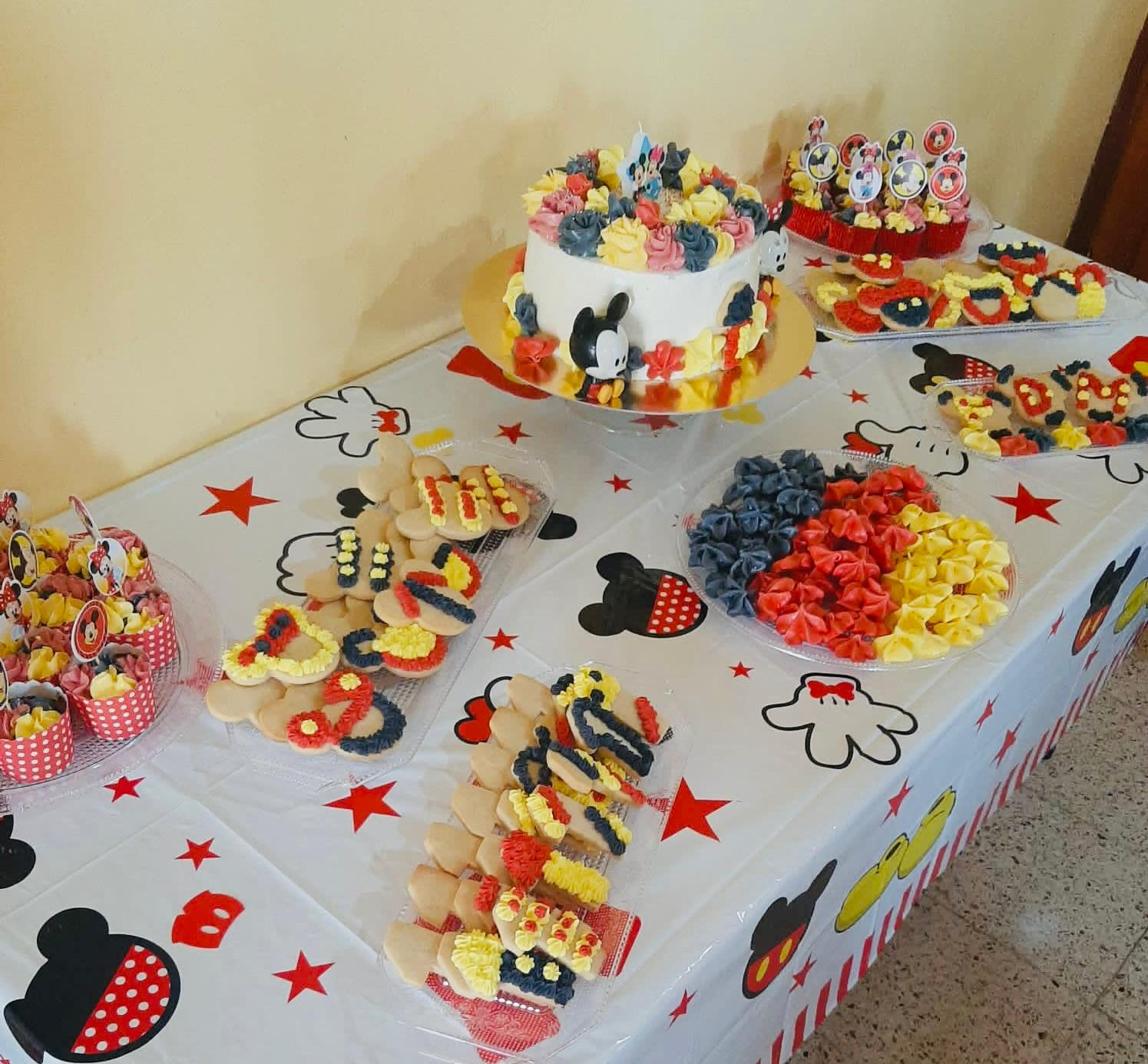 Mesa de postres con pasteles decorados, cupcakes y dulces coloridos sobre un mantel blanco de fiesta.