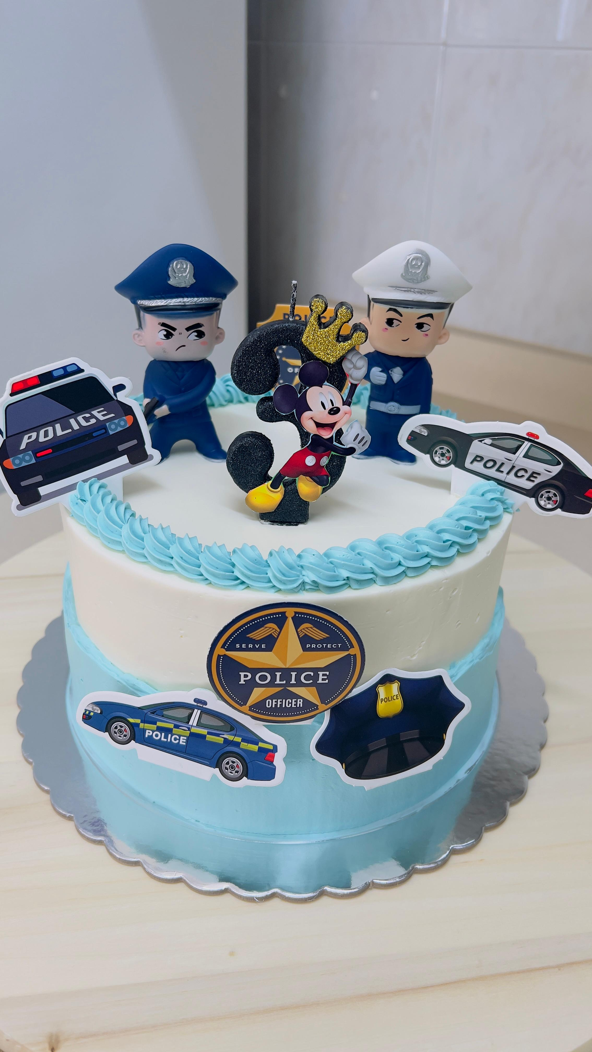 Tarta azul con adornos con temática policial, figuras de dibujos animados e insignias sobre una mesa blanca.