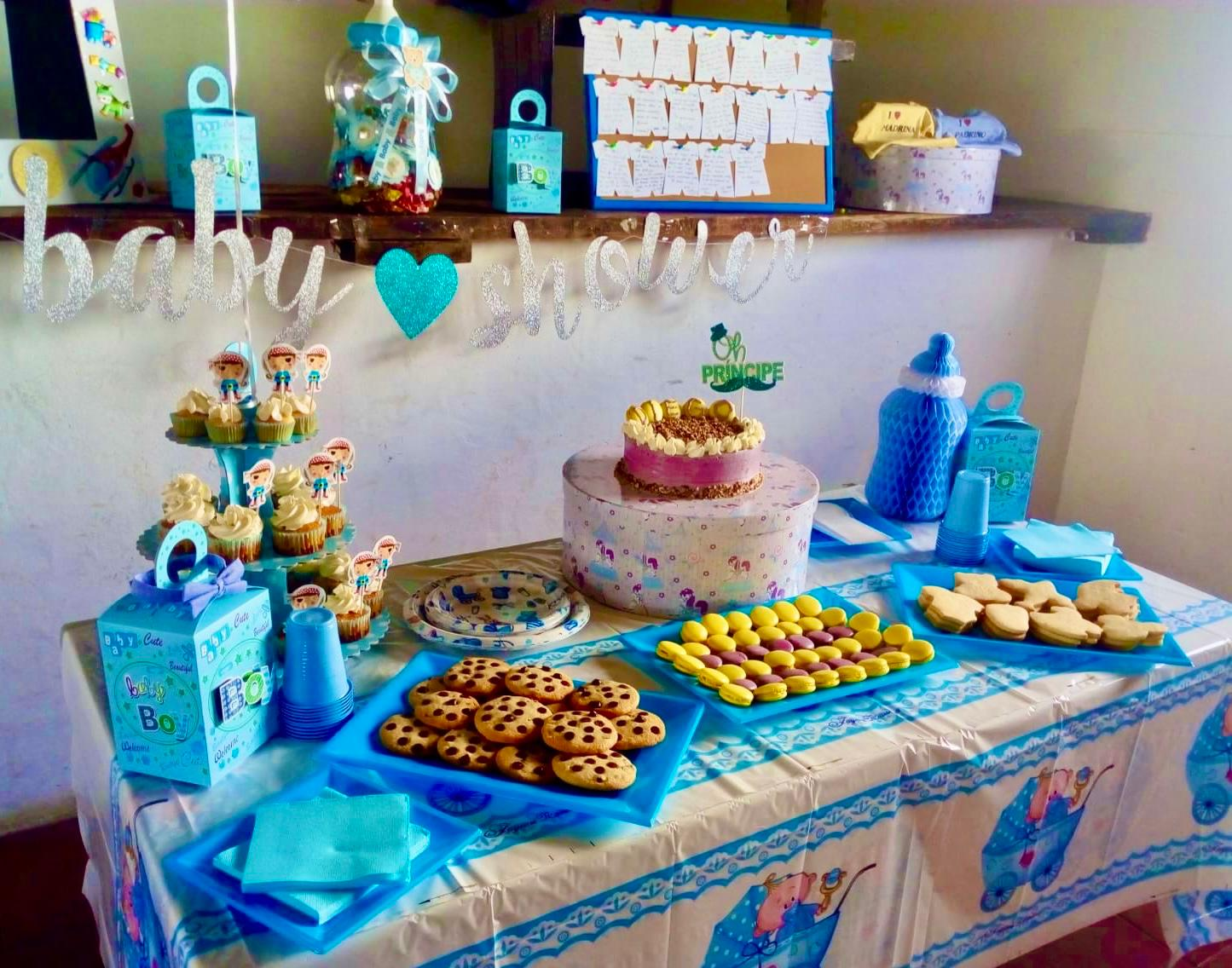 Mesa de postres para baby shower con decoraciones azules y doradas, pastel, cupcakes y galletas.