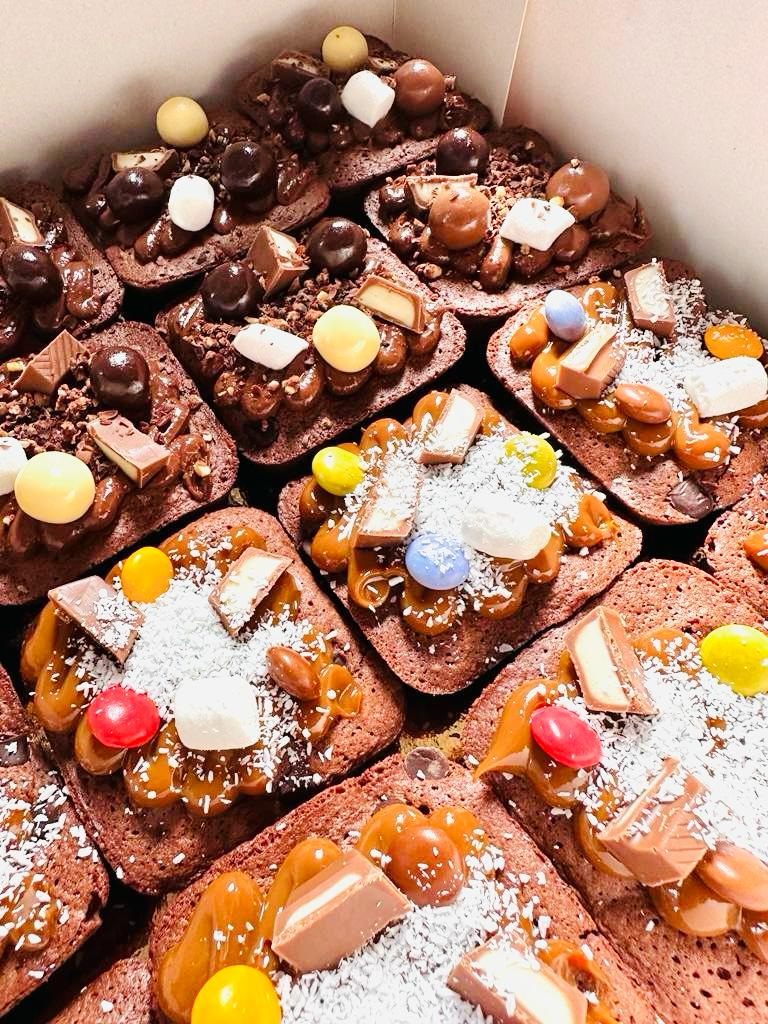 Cuadraditos de postre de chocolate cubiertos con azúcar glas, chispas de chocolate y trozos de caramelo de colores.