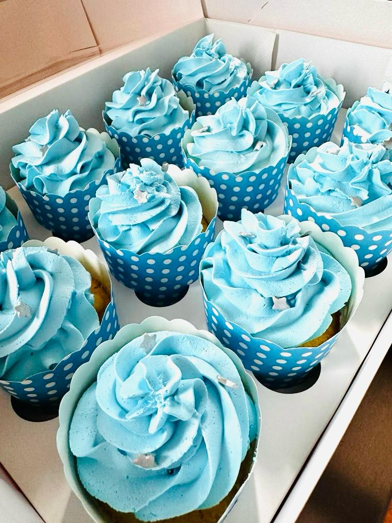 Caja de cupcakes azules glaseados en envoltorios de lunares.
