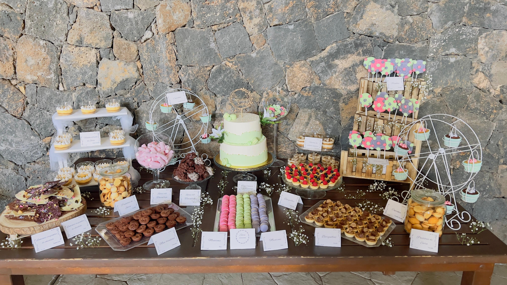 Variedad de postres y pasteles expuestos sobre una mesa junto a una pared de piedra.