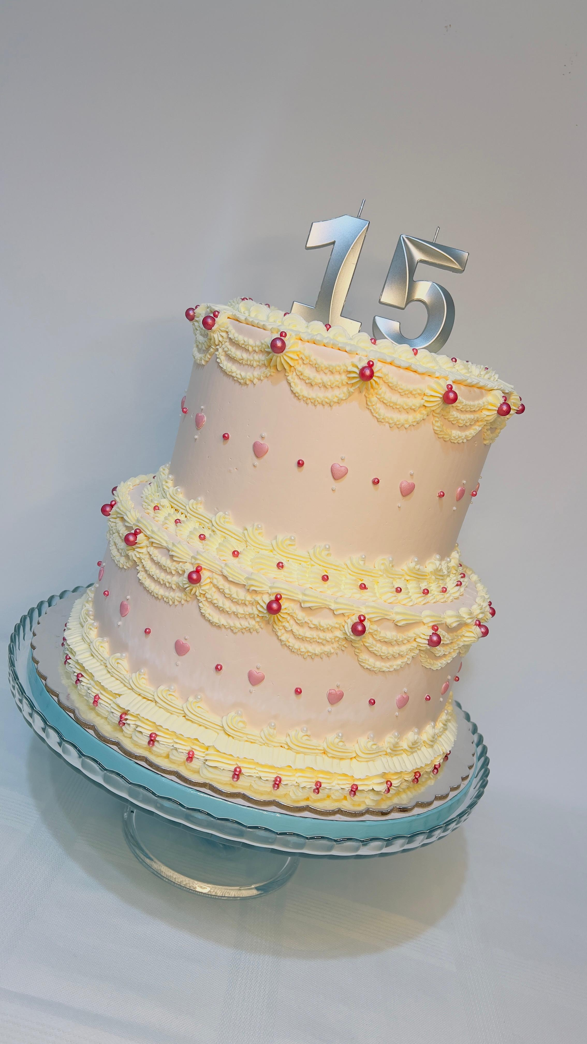 Tarta de cumpleaños de dos pisos en tonos pastel con el número 15 como adorno sobre un soporte azul.