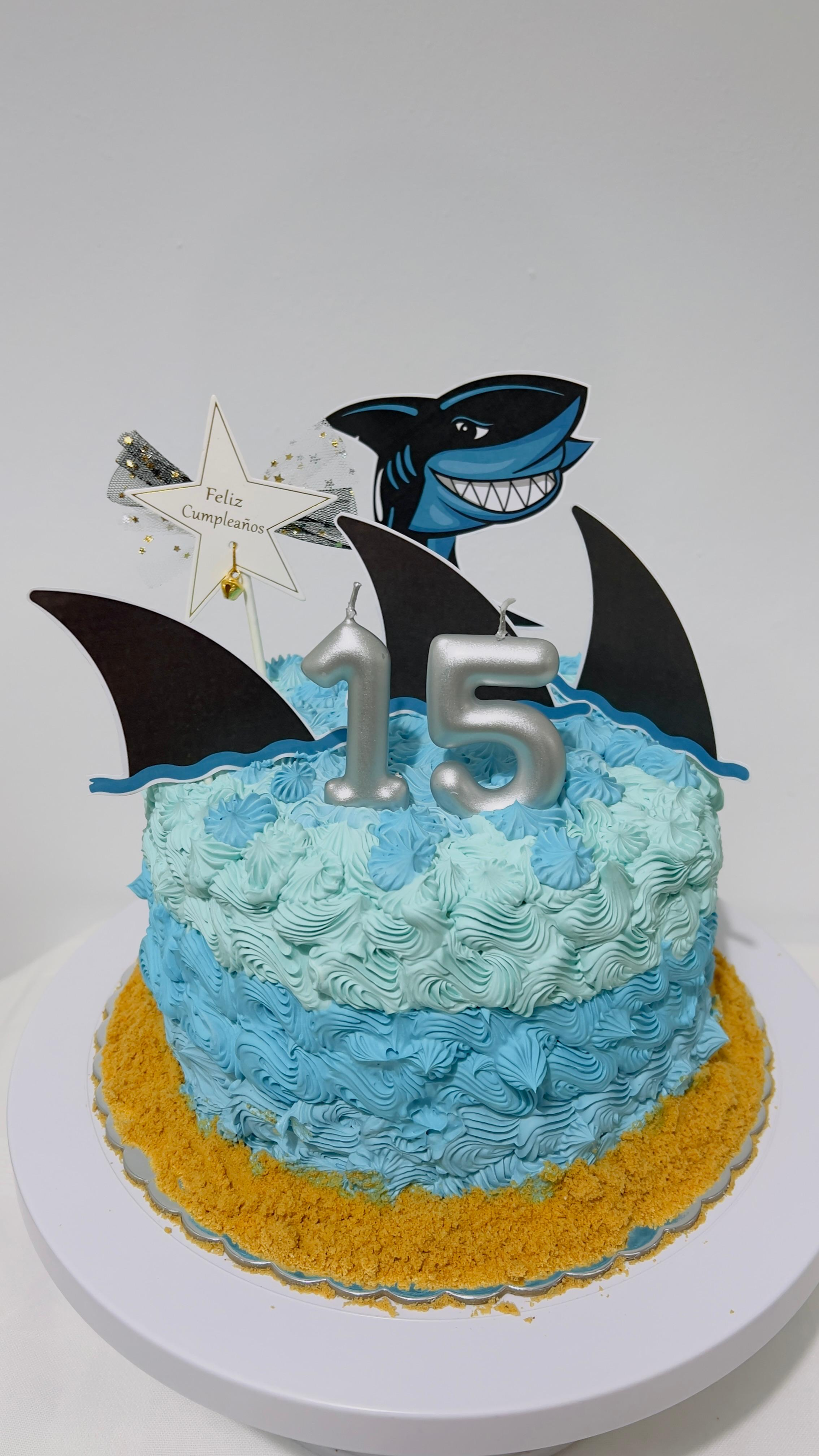 Tarta de cumpleaños azul con adorno de mariposa azul y negra y el número 15 sobre un soporte blanco.