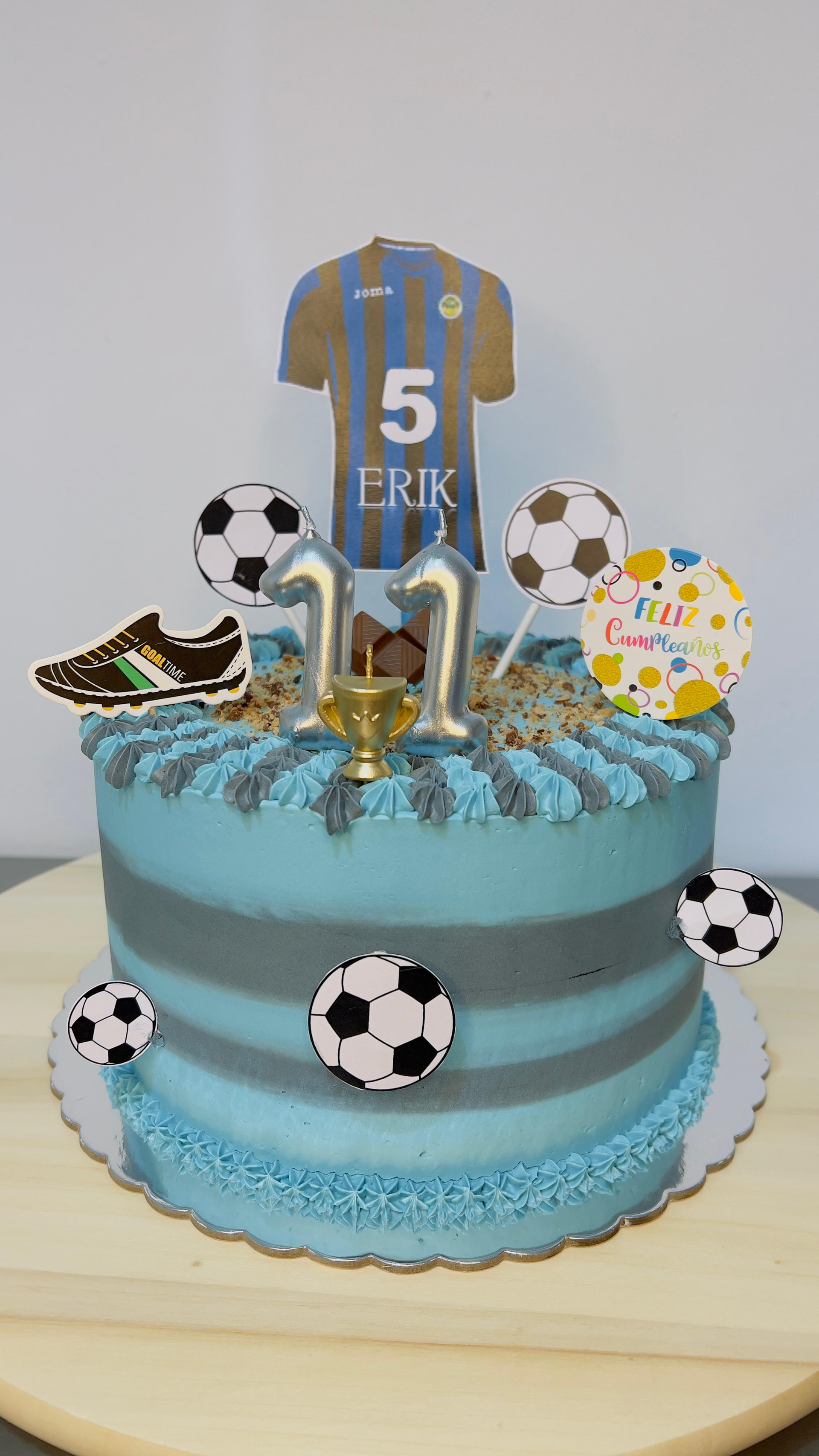 Tarta de cumpleaños azul con temática futbolística, decorada con una camiseta, balones de fútbol y zapatos dorados.