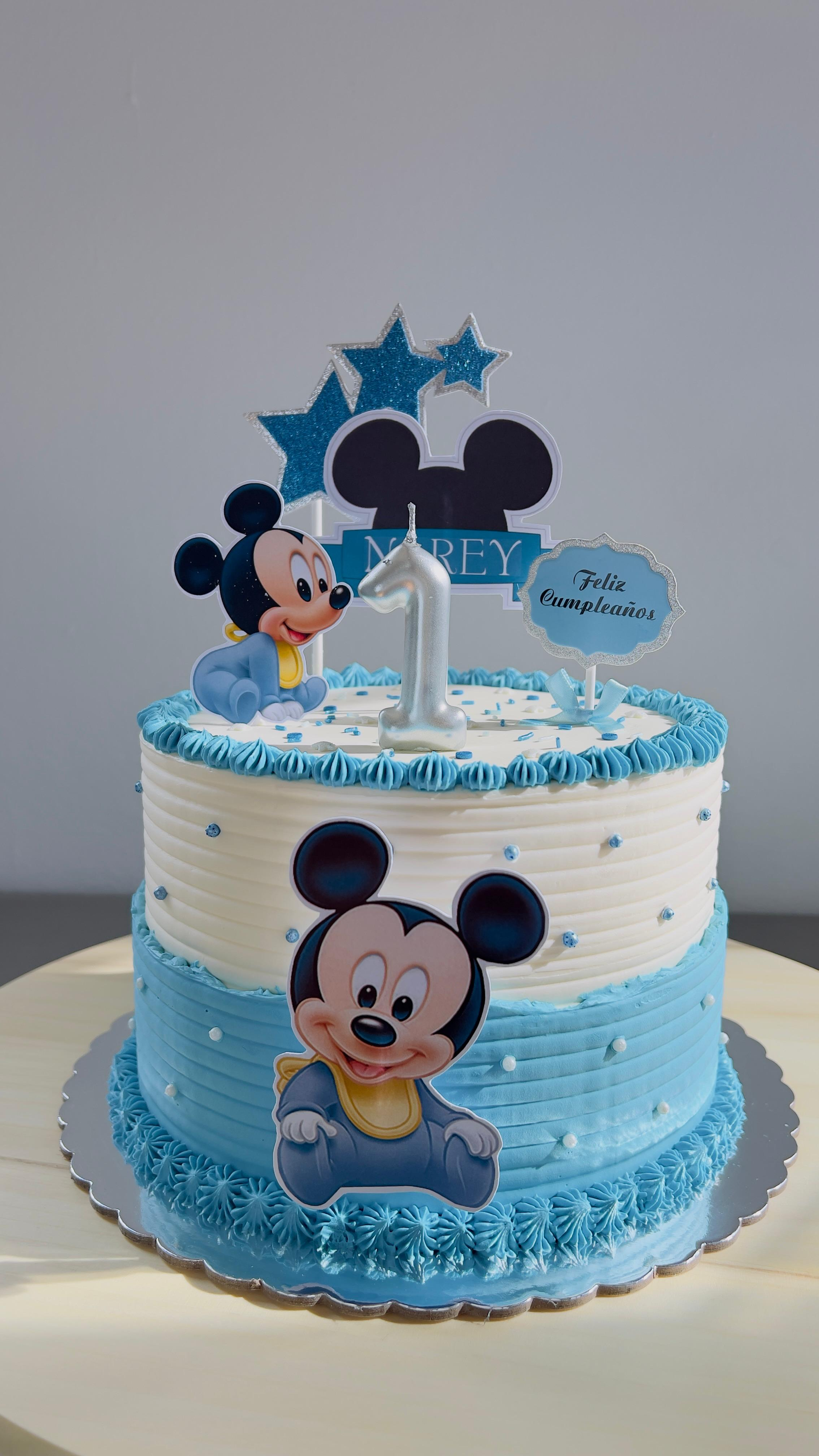 Tarta de cumpleaños azul con temática de Mickey Mouse, decorada con estrellas, nubes y figuras de personajes.