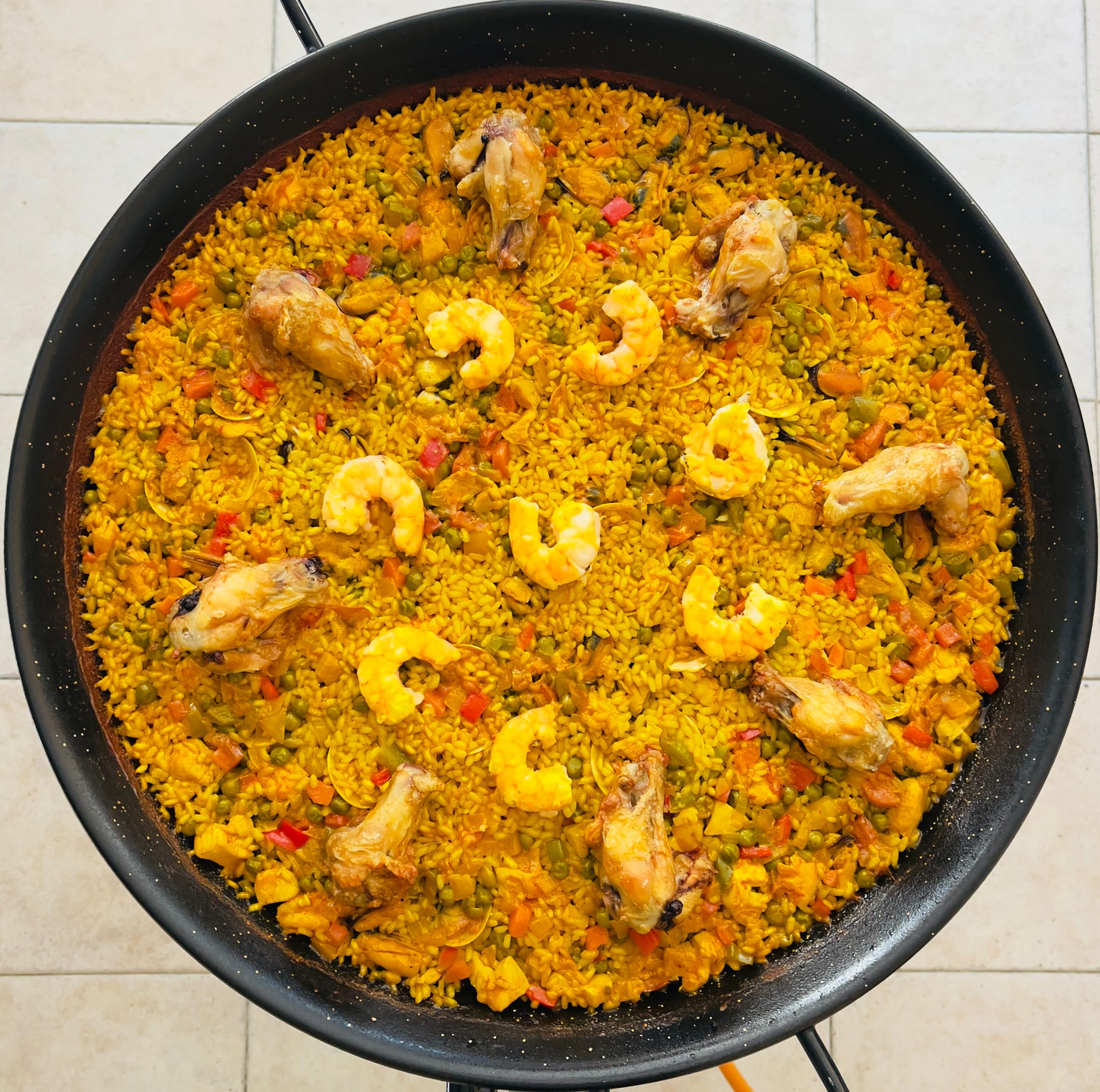 Una olla grande de arroz con azafrán, pollo y camarones, cubierto con pimientos rojos, cocinada en la estufa.