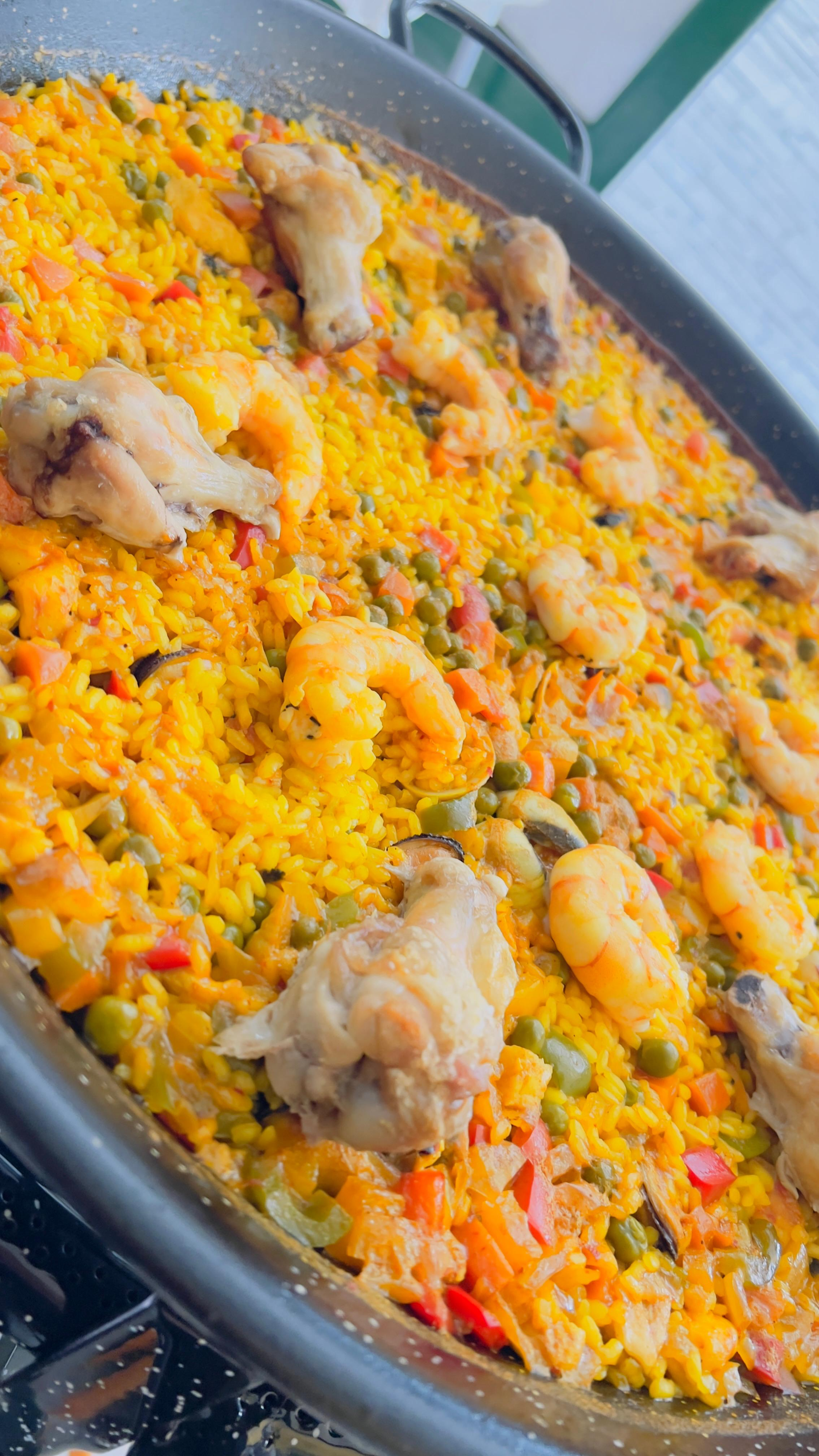 Bandeja de arroz amarillo con trozos de pollo y verduras en dados, servida en una sartén redonda grande.