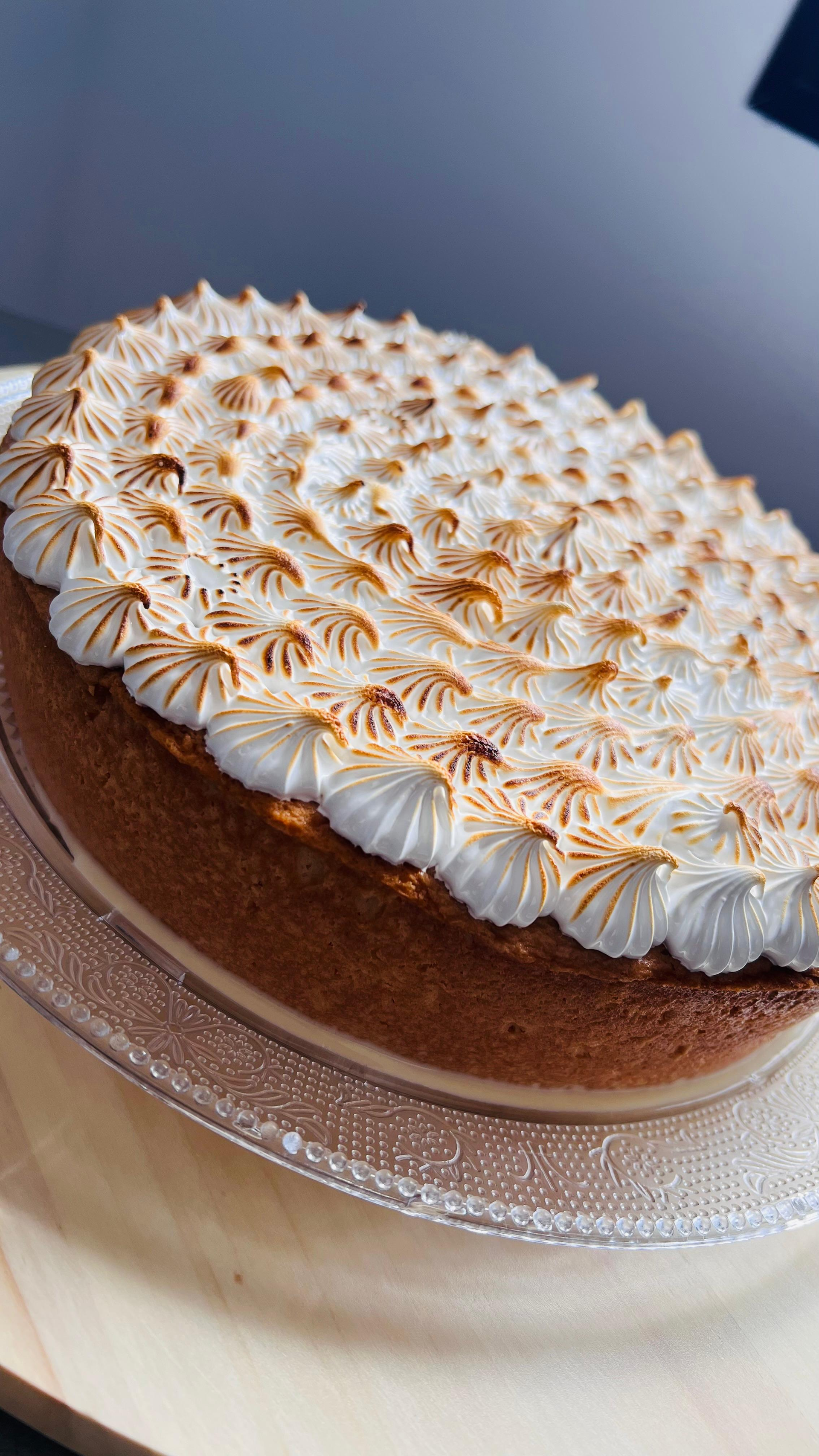 Pastel redondo decorado con espirales de merengue blanco y caramelo sobre un soporte de cristal.