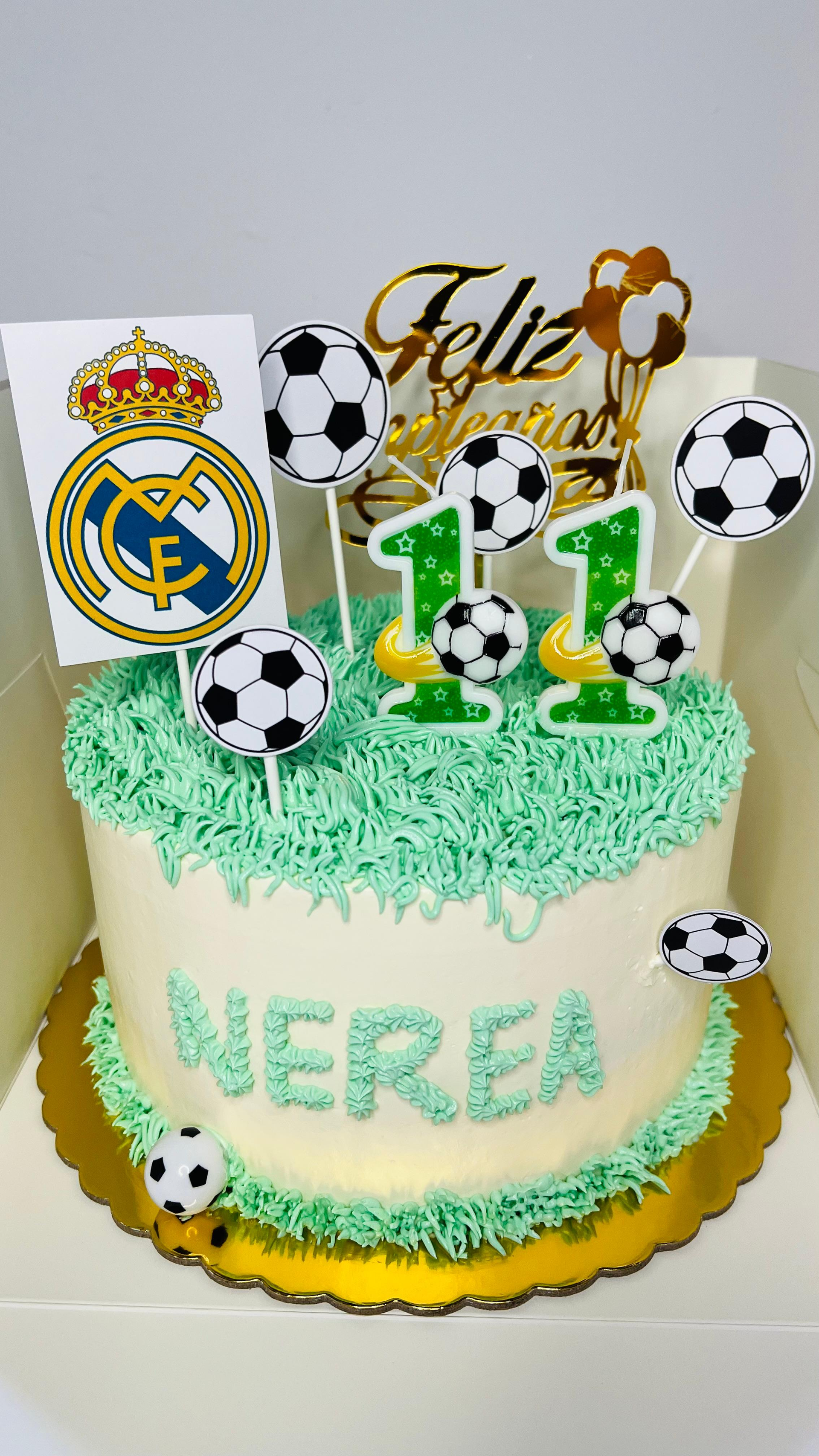 Tarta de cumpleaños con temática de fútbol, ​​con glaseado verde, base blanca y decoración de balones blancos y negros.