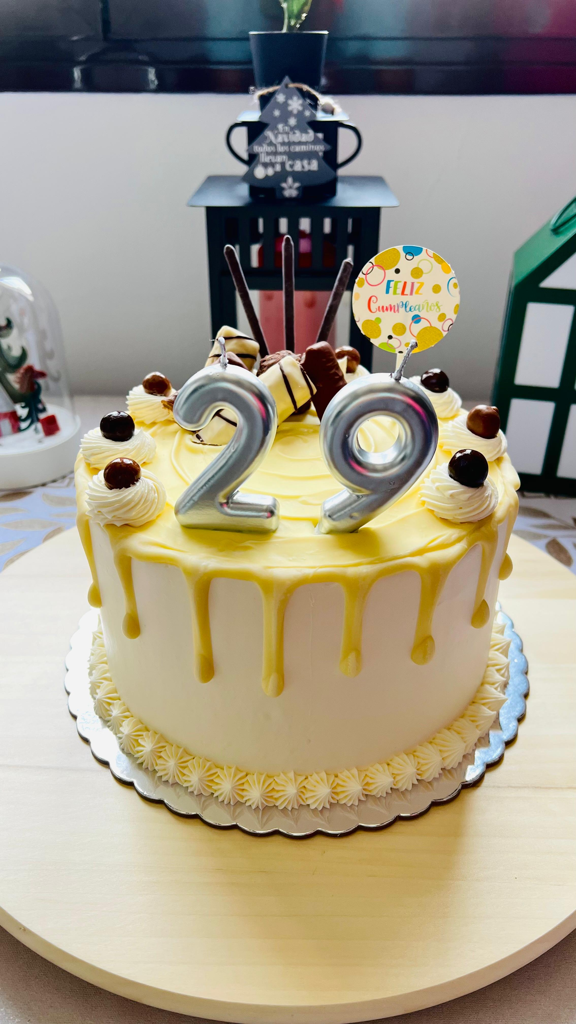 Tarta de cumpleaños blanca con glaseado amarillo que gotea y adorno plateado con el número 