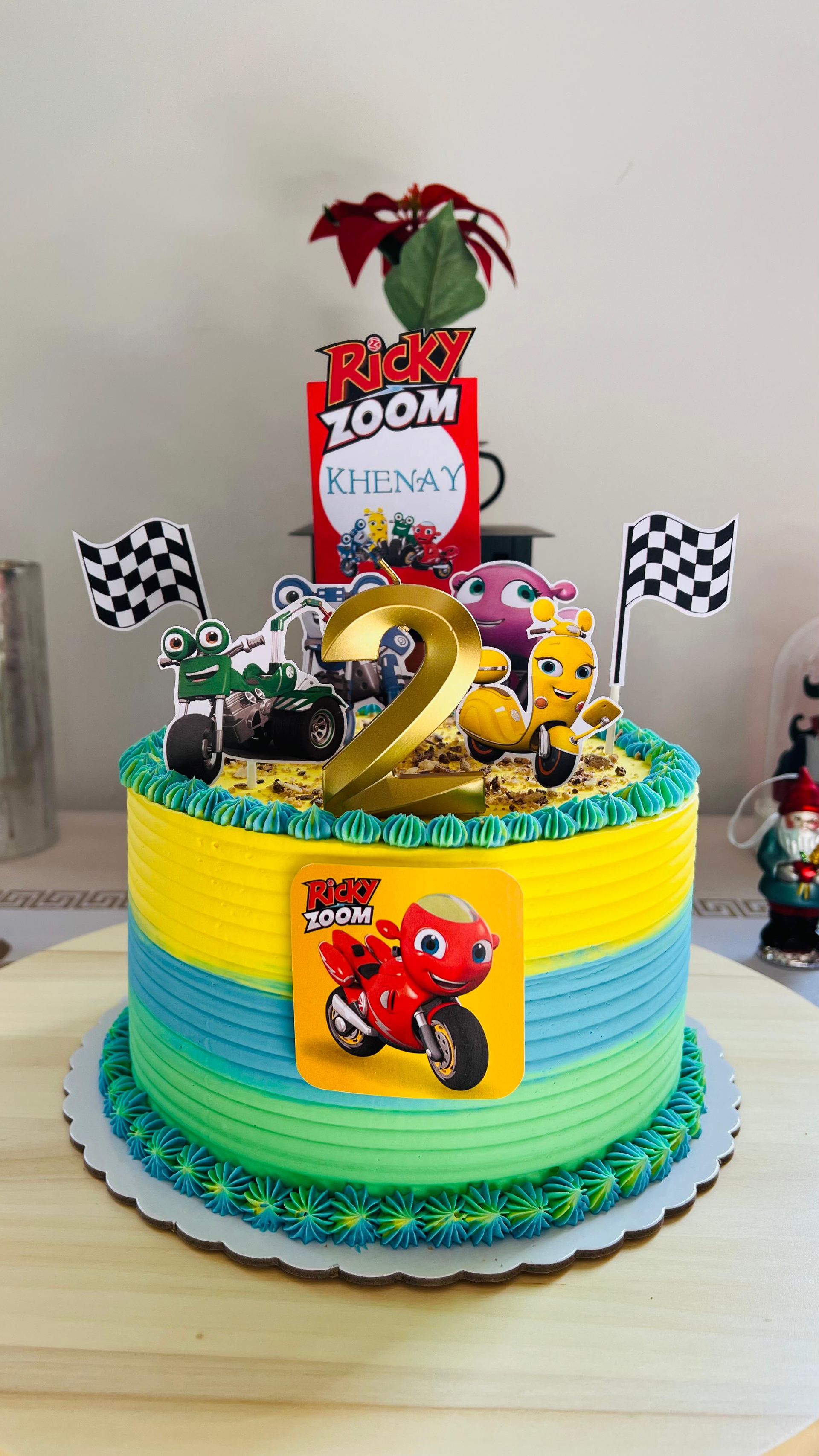 Tarta de cumpleaños con forma de camión monstruo, colorida, con banderas a cuadros, un número 2 dorado.