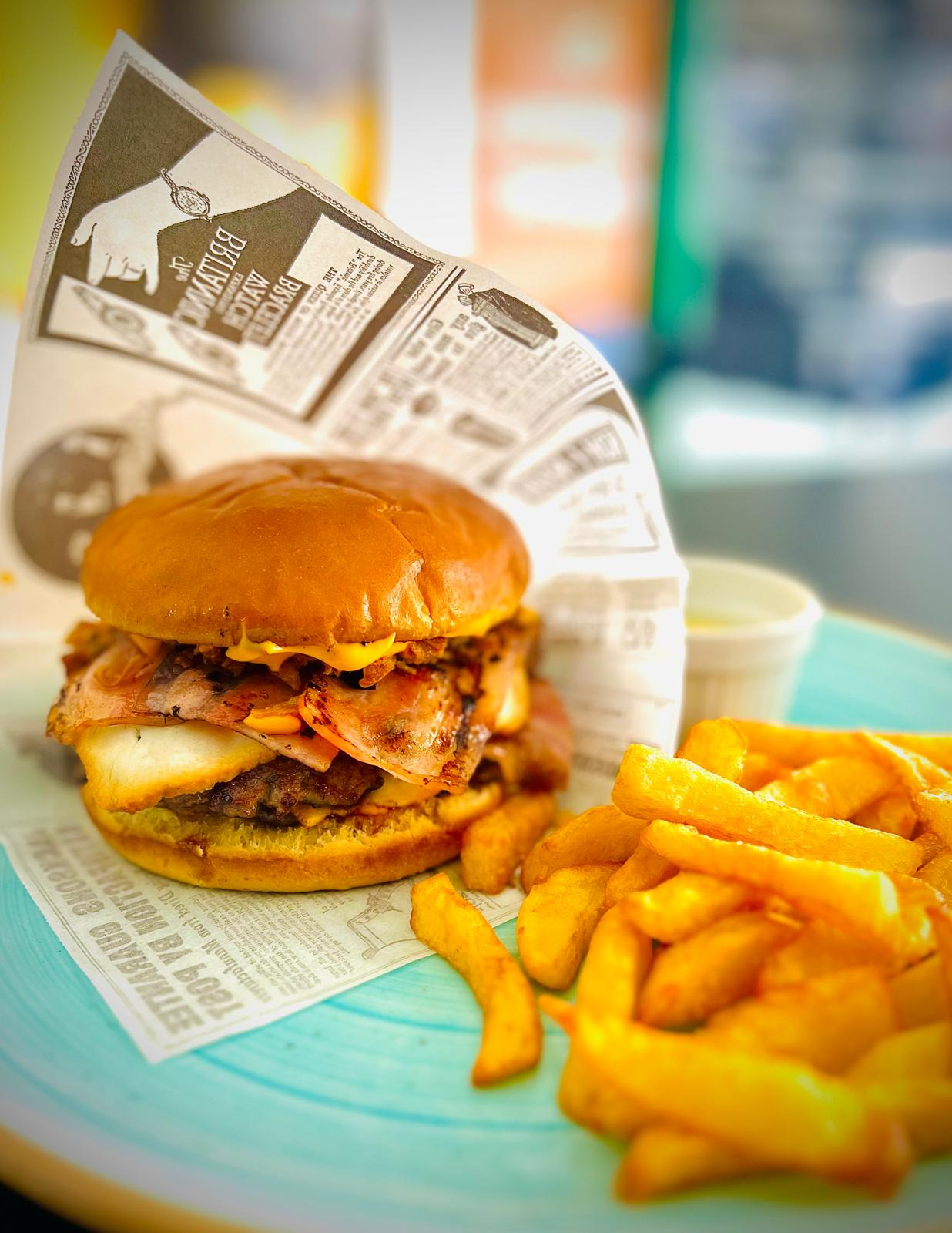 Hamburguesa y patatas fritas en una bandeja forrada con papel, con un plato turquesa al fondo.