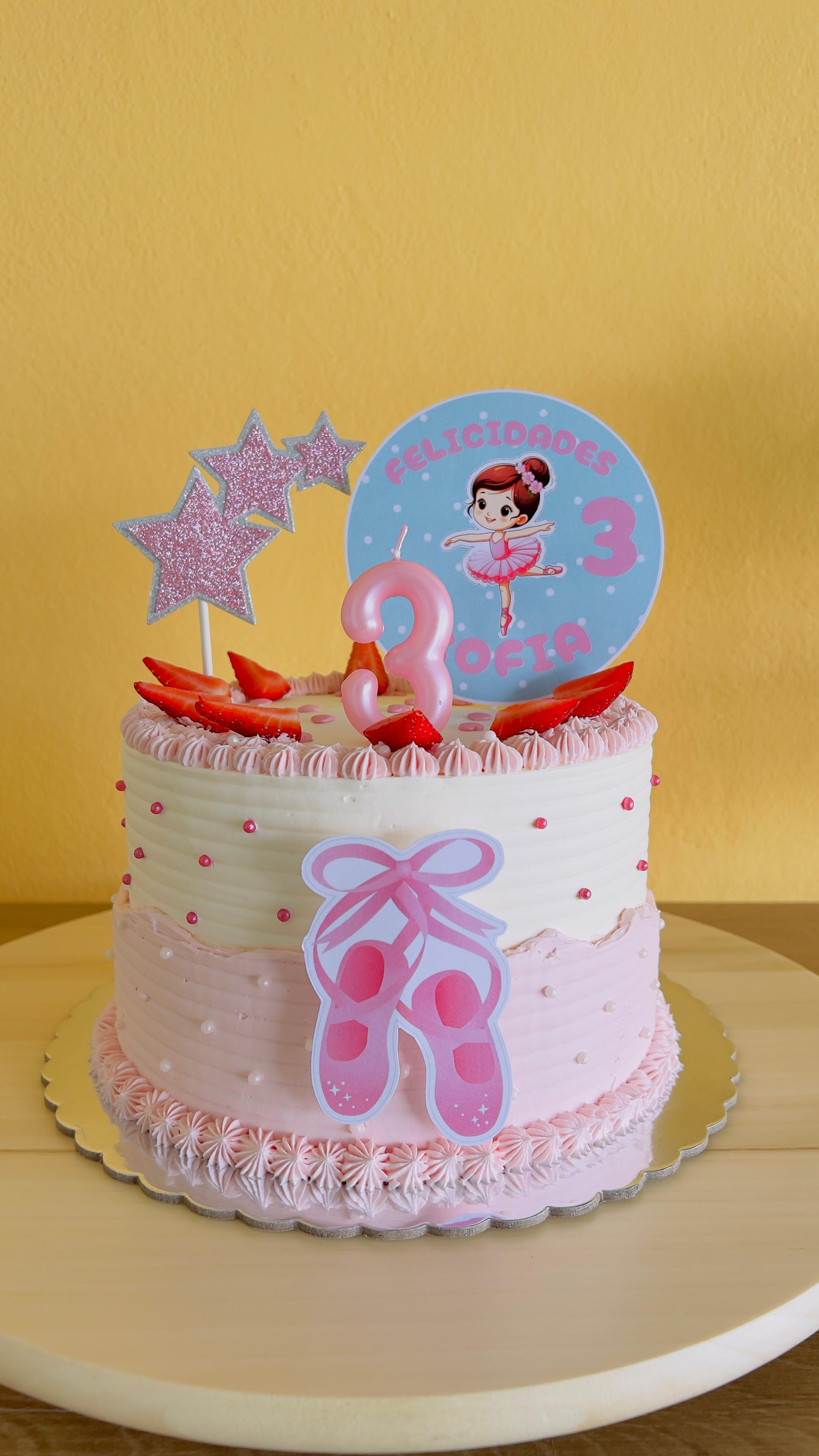 Tarta de cumpleaños rosa con adorno de bailarina, estrellas y decoraciones de cintas sobre un soporte.