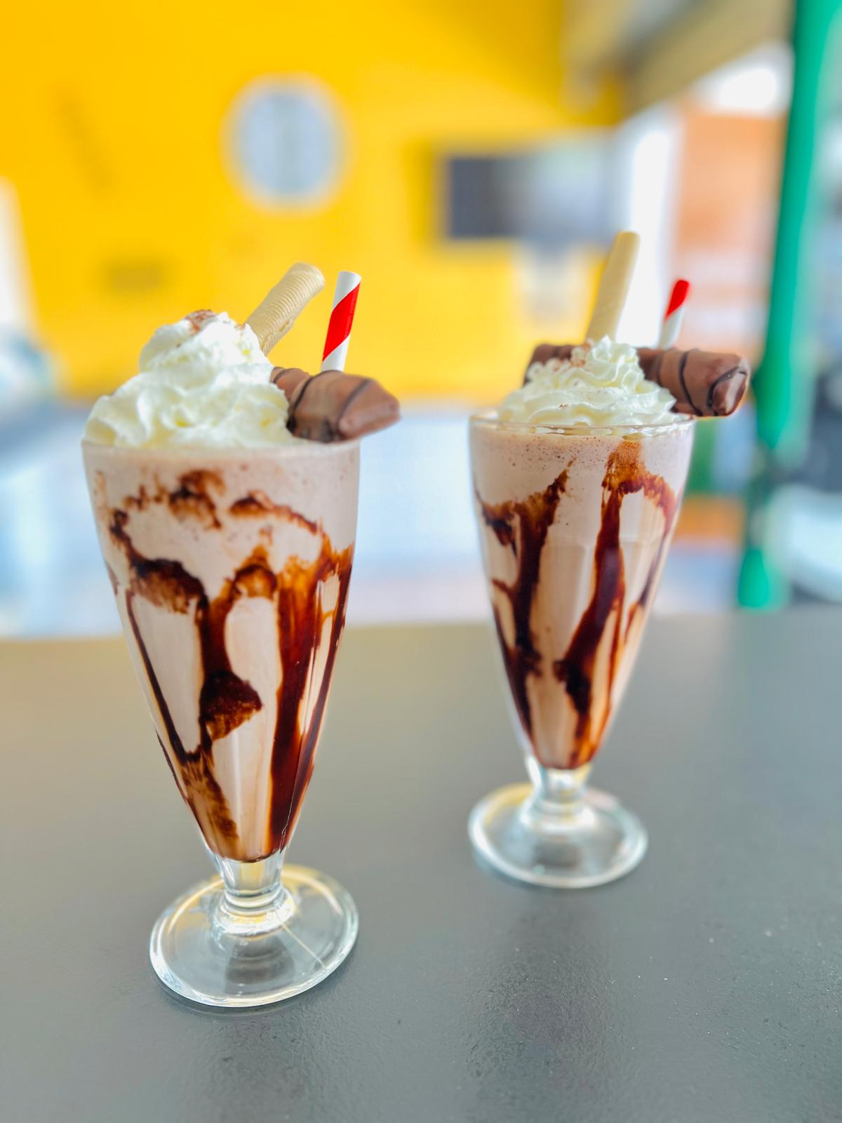 Dos batidos de chocolate con nata montada en vasos altos sobre una mesa.