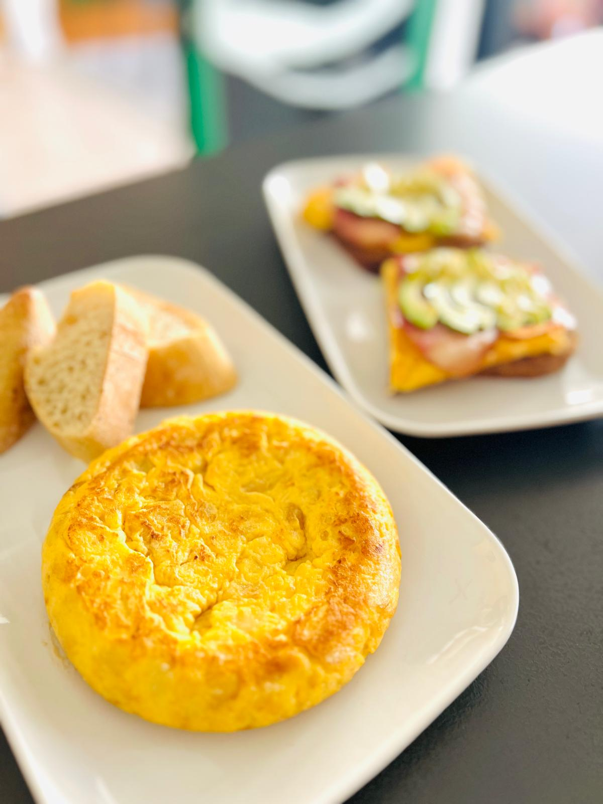 Platos de desayuno con tortilla, tostada y tostada de aguacate sobre una mesa.
