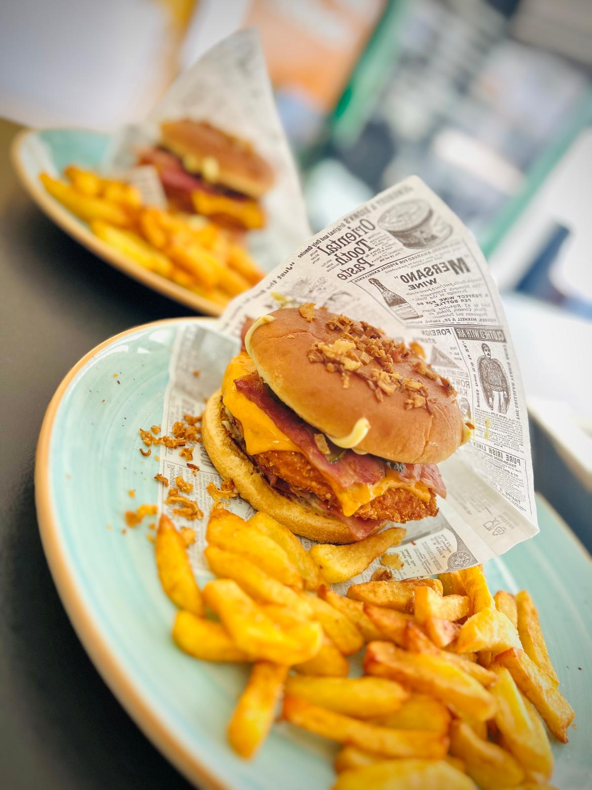 Hamburguesa y patatas fritas en una bandeja forrada con papel en una mesa de un restaurante informal.