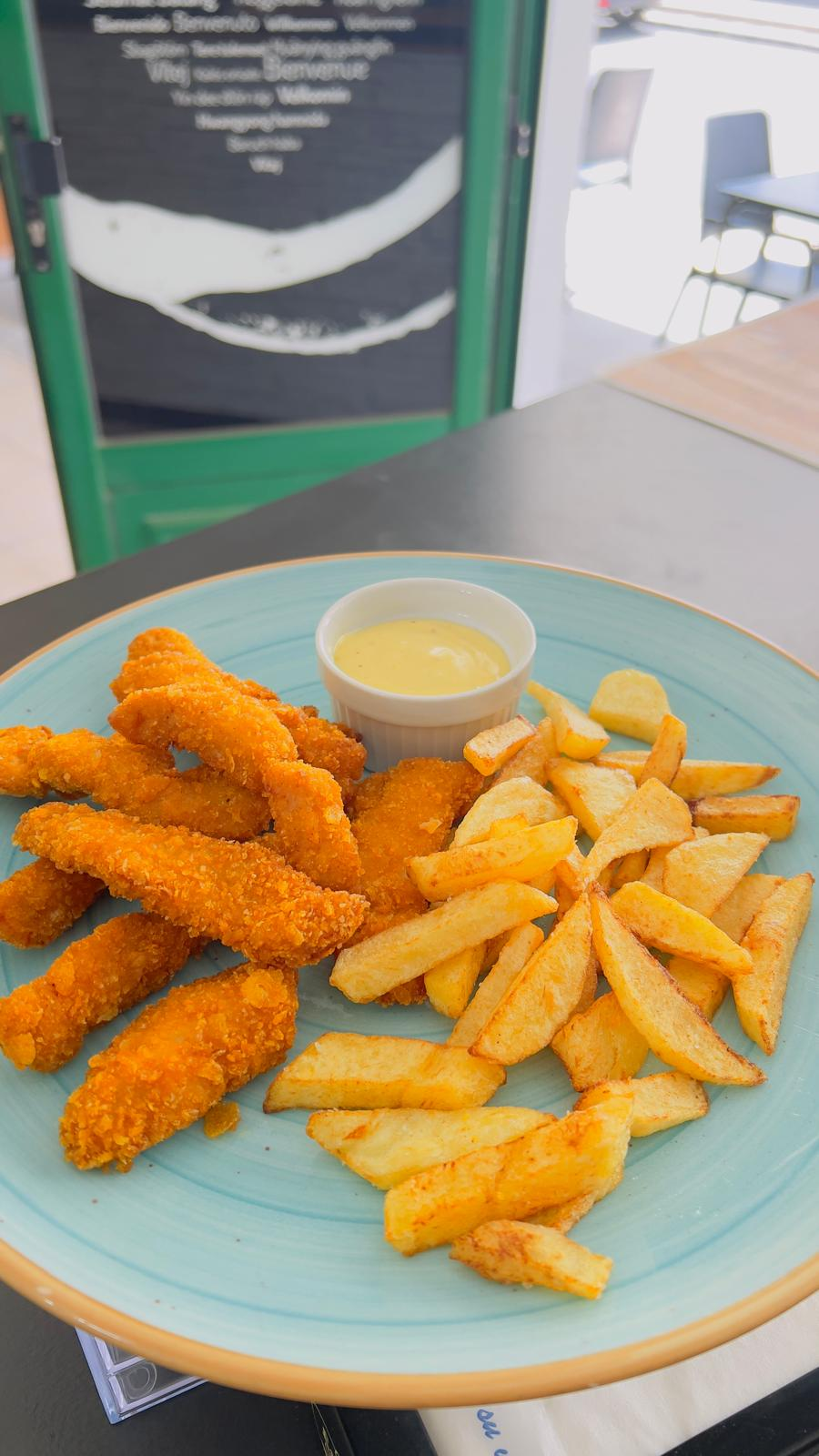 Plato de tiras de pollo frito, papas fritas y salsa para mojar en un plato azul.
