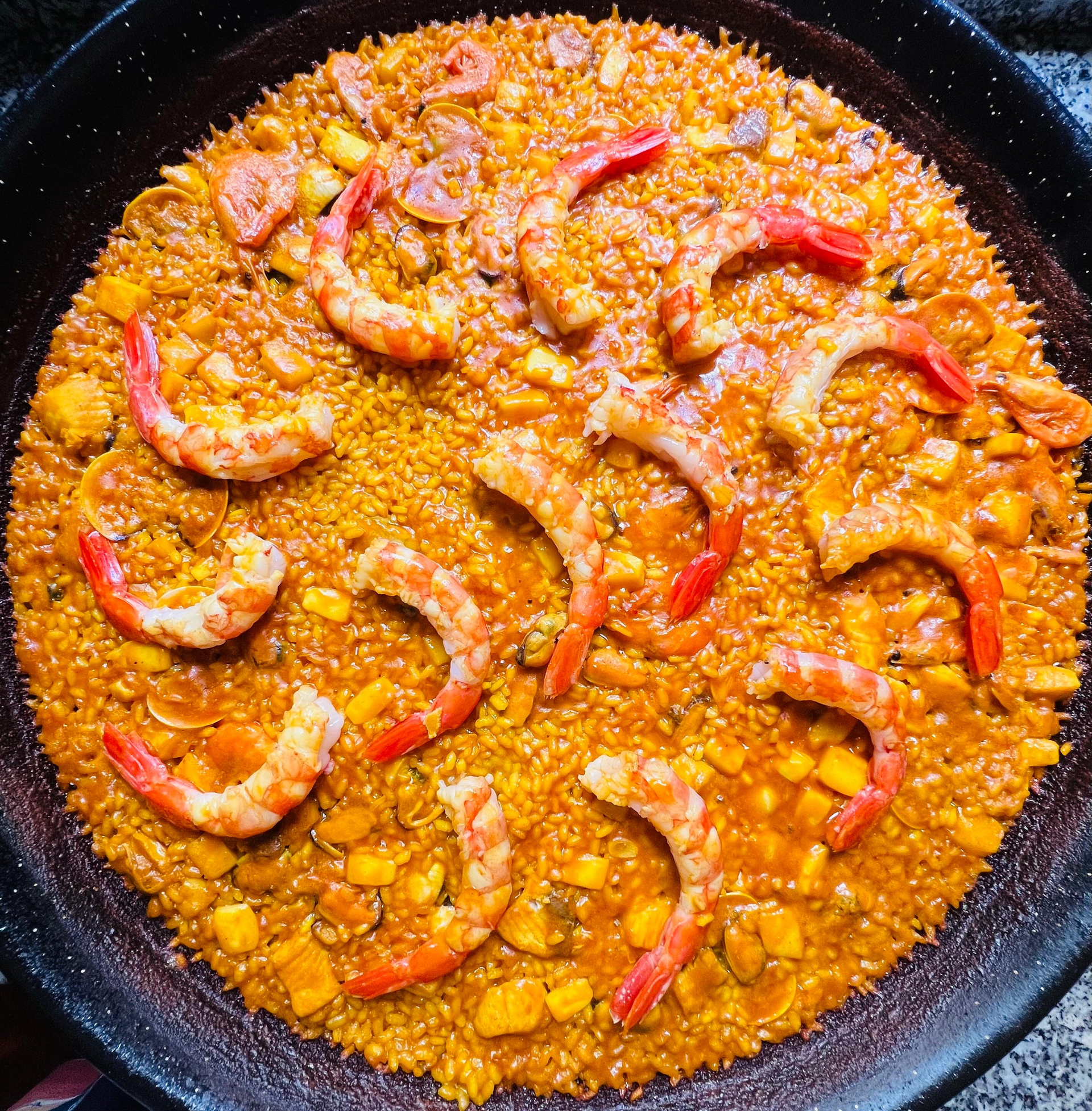 Paella de gambas con rodajas de pimiento rojo en una sartén negra.