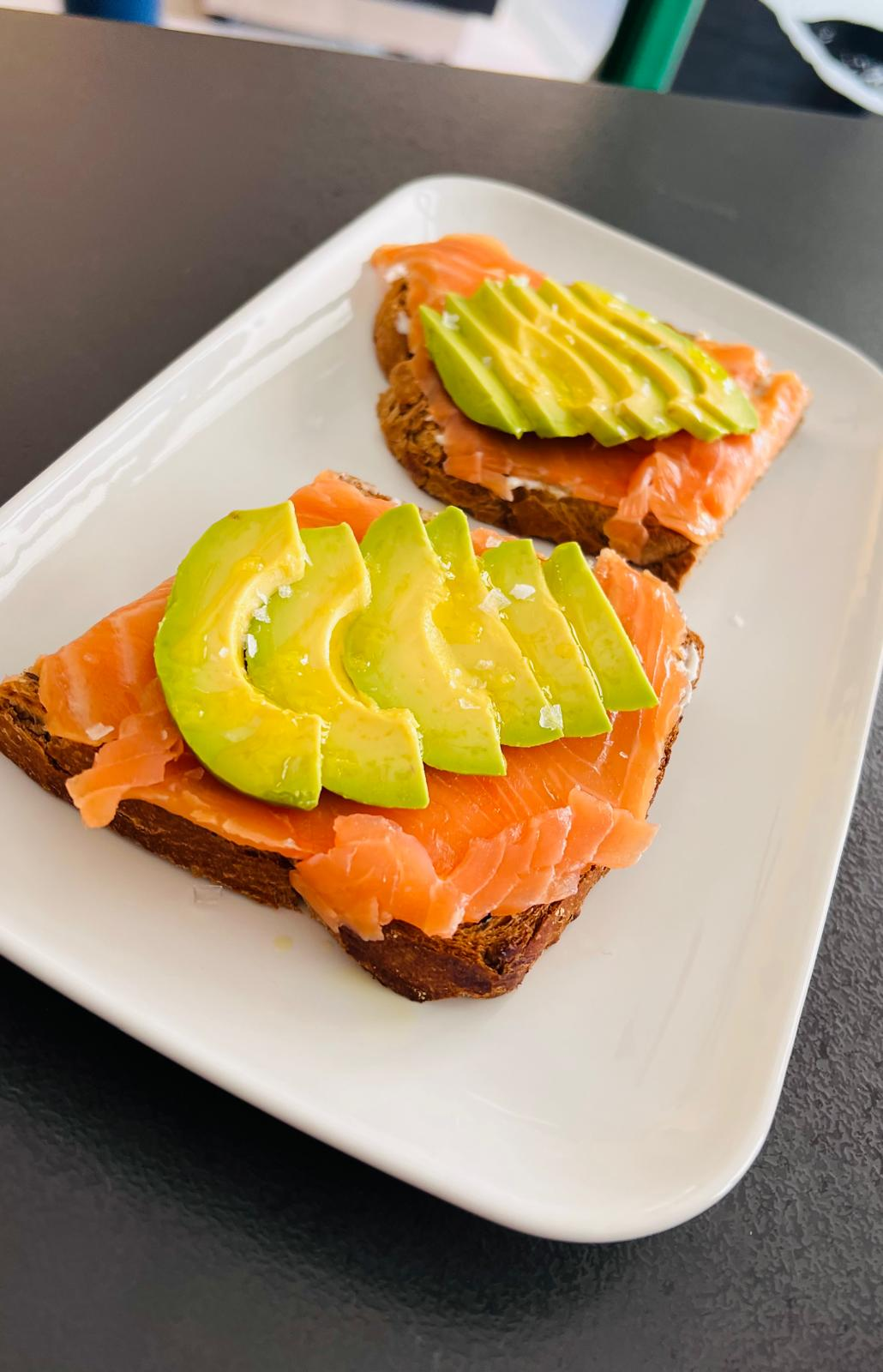 Dos tostadas de aguacate y salmón en un plato blanco, adornadas con rodajas de limón.