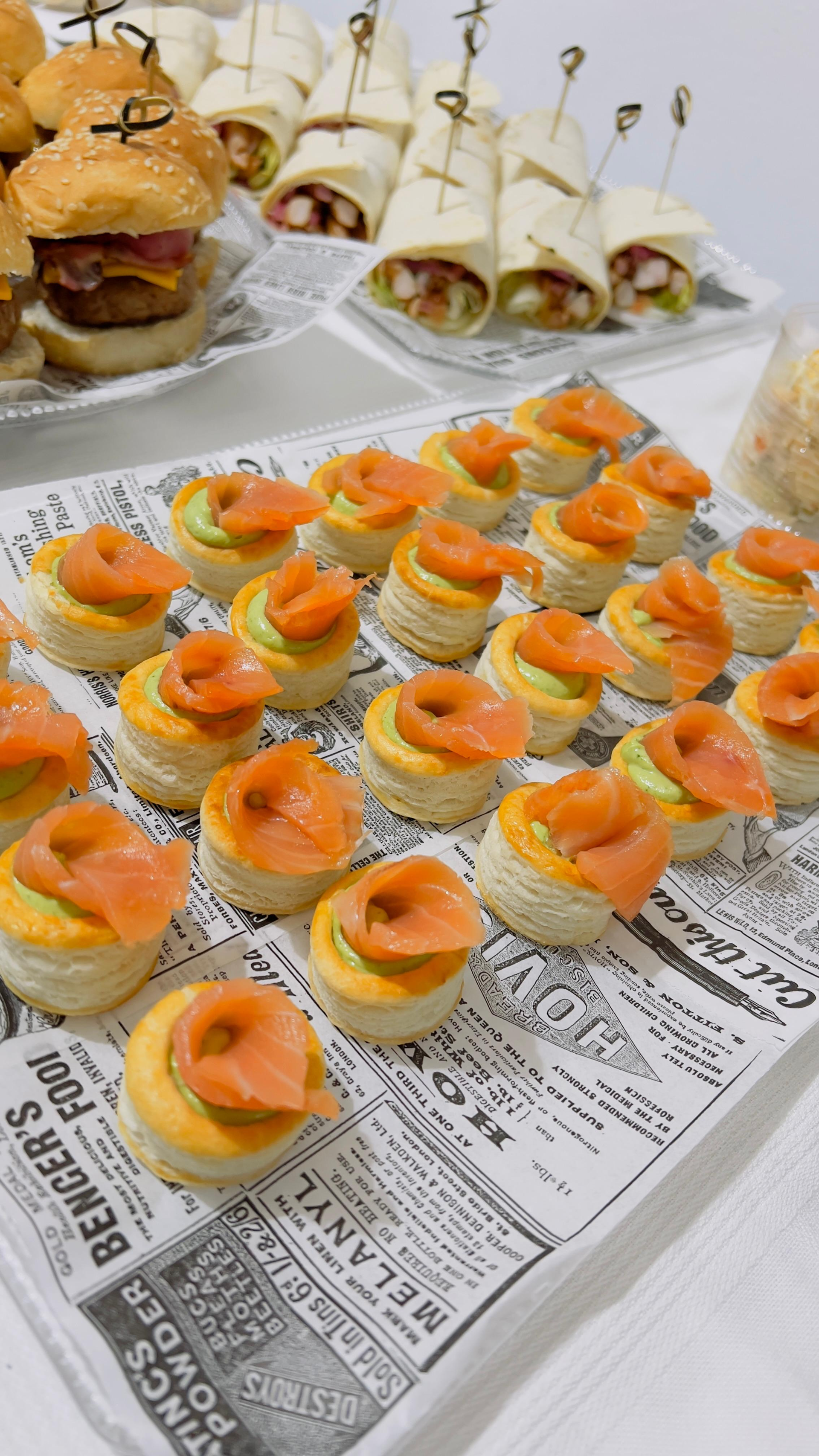 Variedad de aperitivos pequeños con cobertura de naranja envueltos en papel tipo periódico en una mesa de buffet.