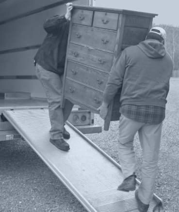 Zwei Männer tragen eine Kommode aus einem Lastwagen.