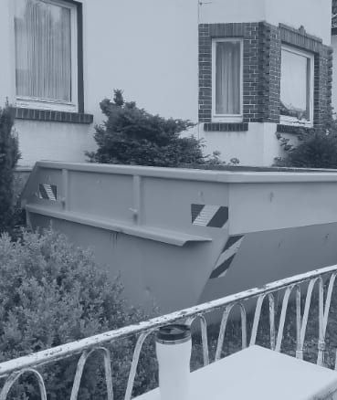 Ein Schwarzweißfoto eines Müllcontainers vor einem Haus.