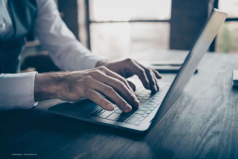 Seitenansicht eines schwarzen aufgeklappten Laptops mit zwei Männerhänden auf der Tastatur