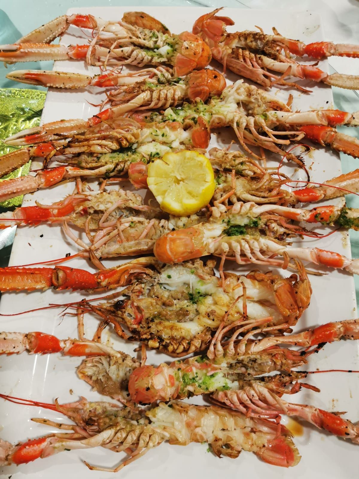 Una bandeja de langostinos cocidos, de color naranja rojizo, dispuestos alrededor de una rodaja de limón, listos para comer.