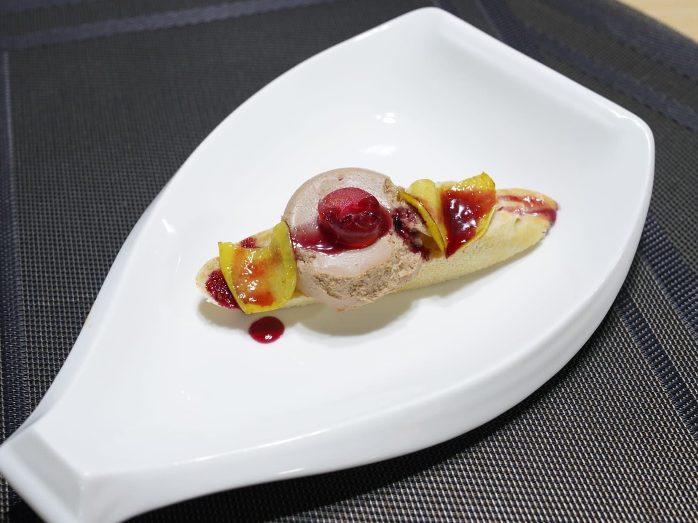 Un postre con una bola de helado de chocolate, frambuesas y rodajas de mango, servido en un plato blanco en forma de barco.