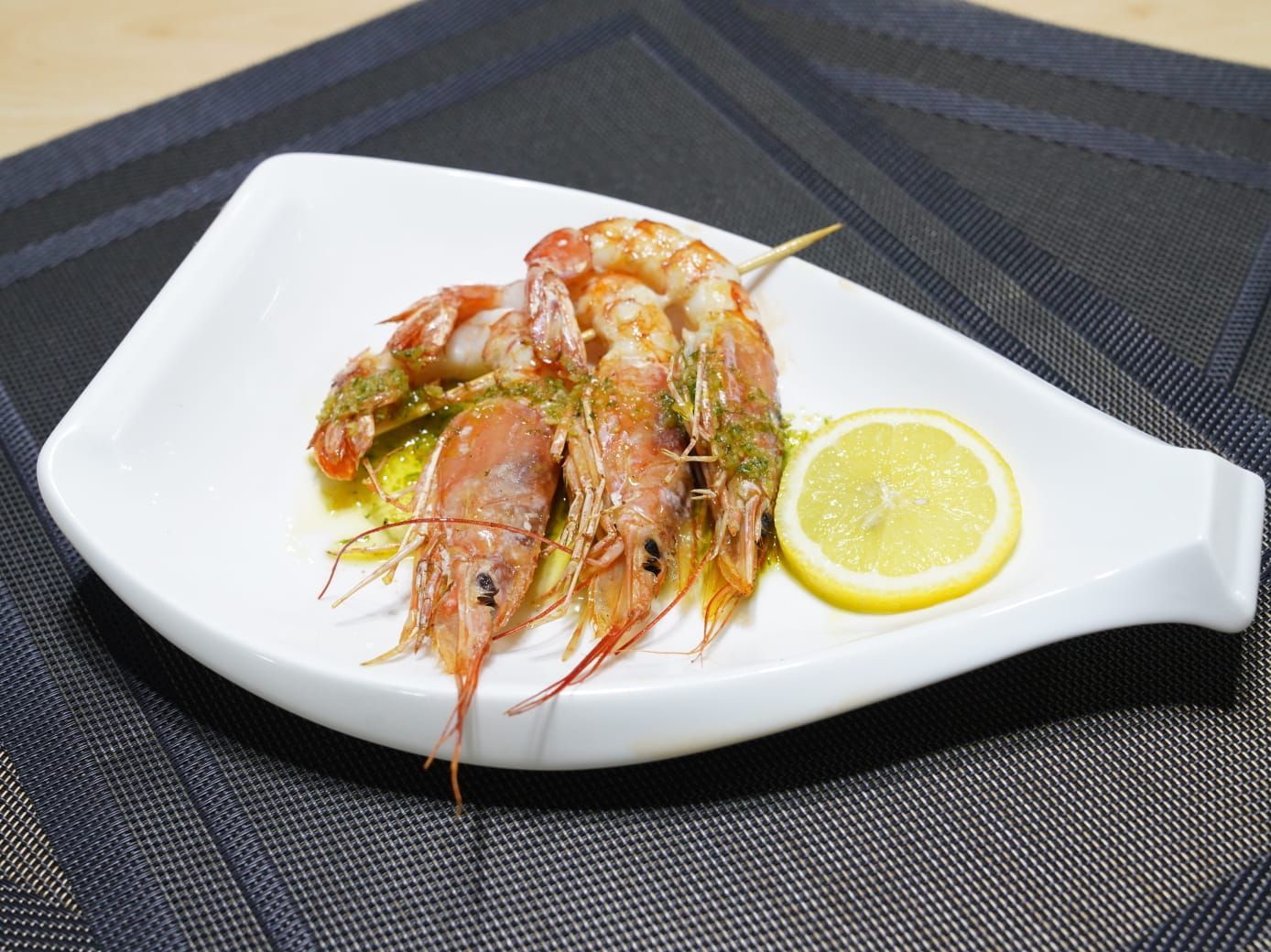 Camarones cocidos en un plato blanco con una rodaja de limón, colocados sobre un mantel azul oscuro.