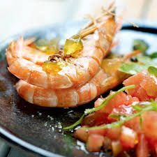 Camarones a la parrilla con gajos de naranja y hierbas en un plato oscuro.