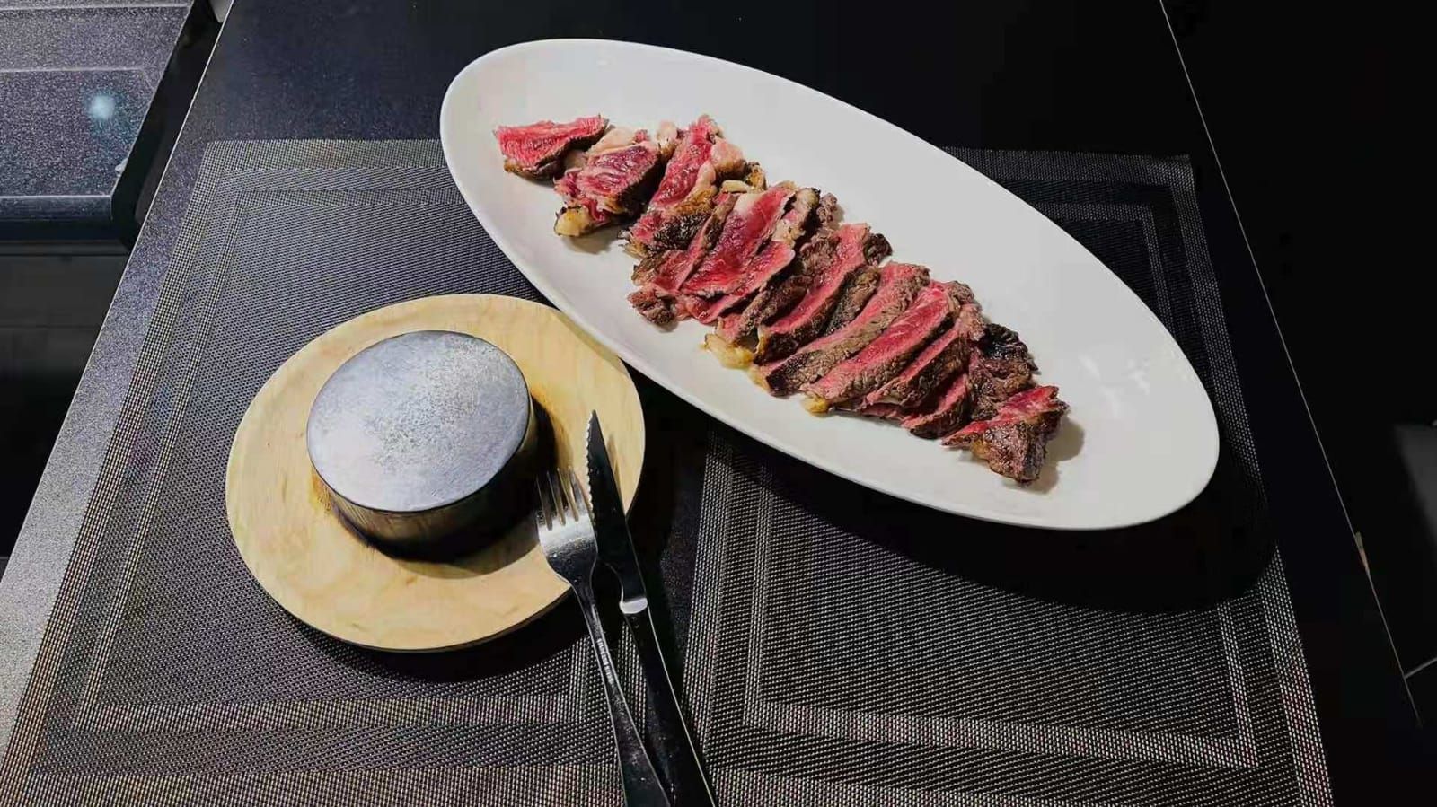 Filete cortado en rodajas en un plato ovalado blanco, servido con una guarnición de salsa y cubiertos sobre un mantel individual texturizado.