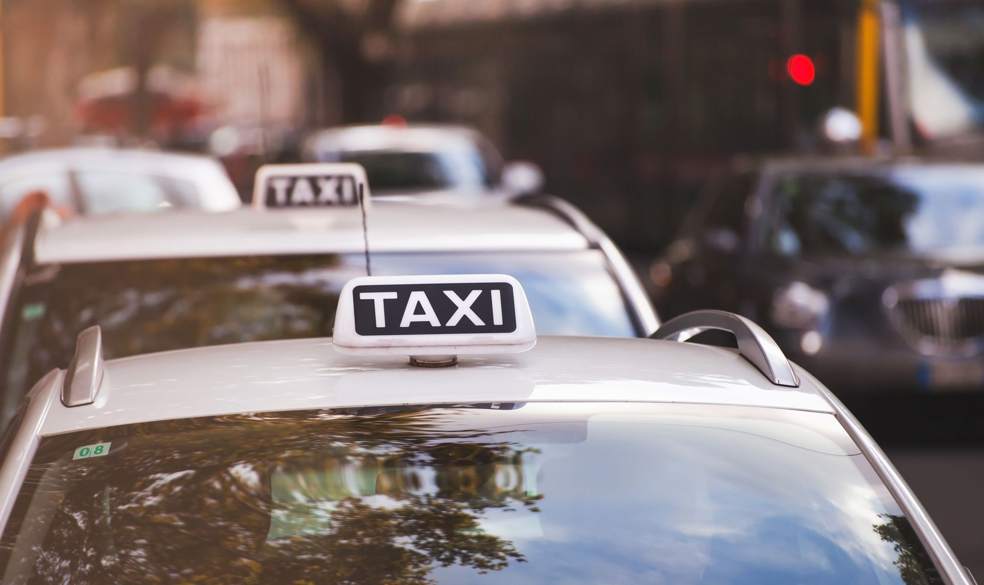 Plusieurs taxis argentés dans la circulation, gros plan sur l'enseigne lumineuse du taxi sur le toit du premier véhicule.