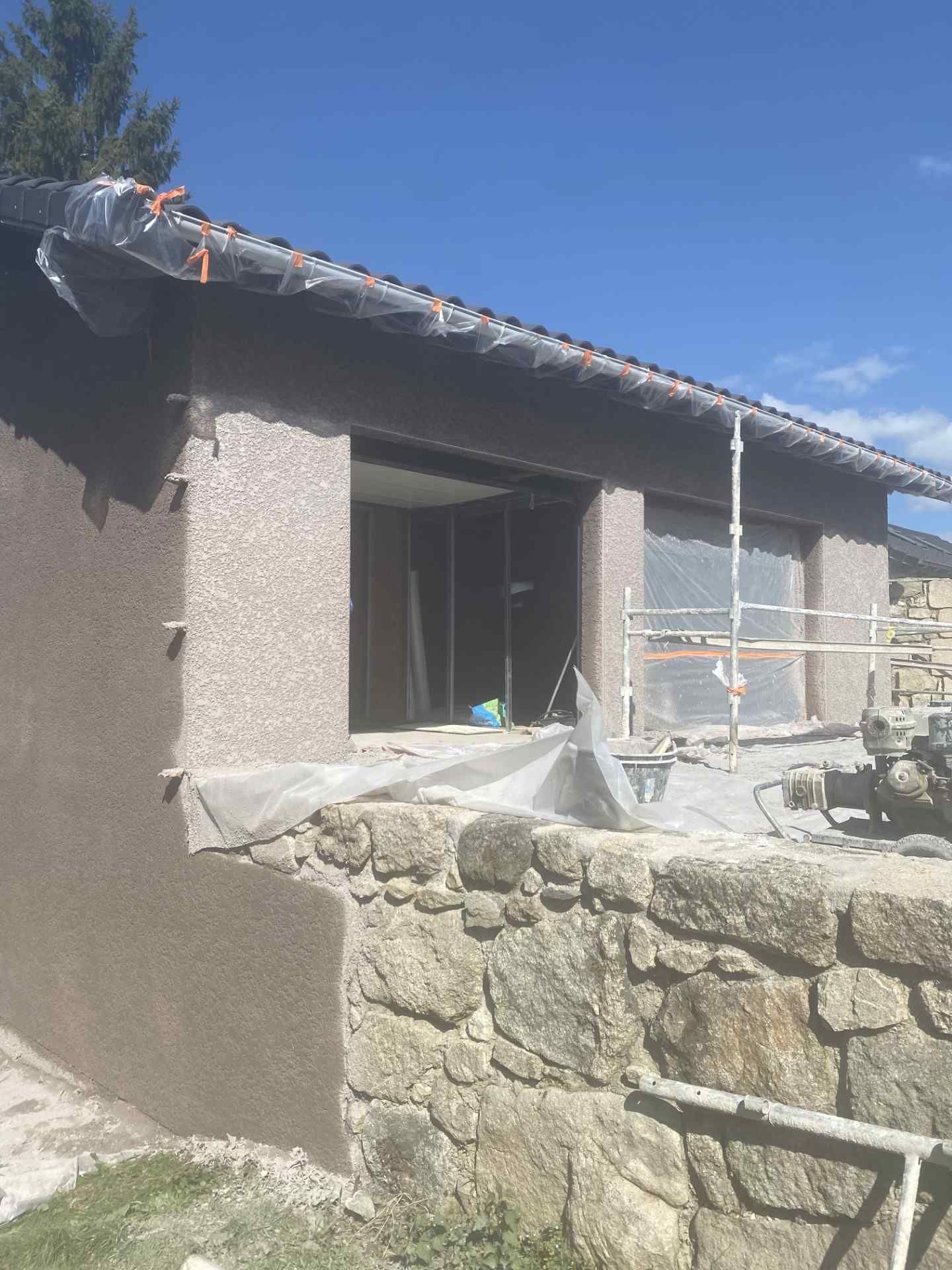Maison en pierre partiellement achevée, avec un toit recouvert d'une bâche et des matériaux de construction à l'extérieur.
