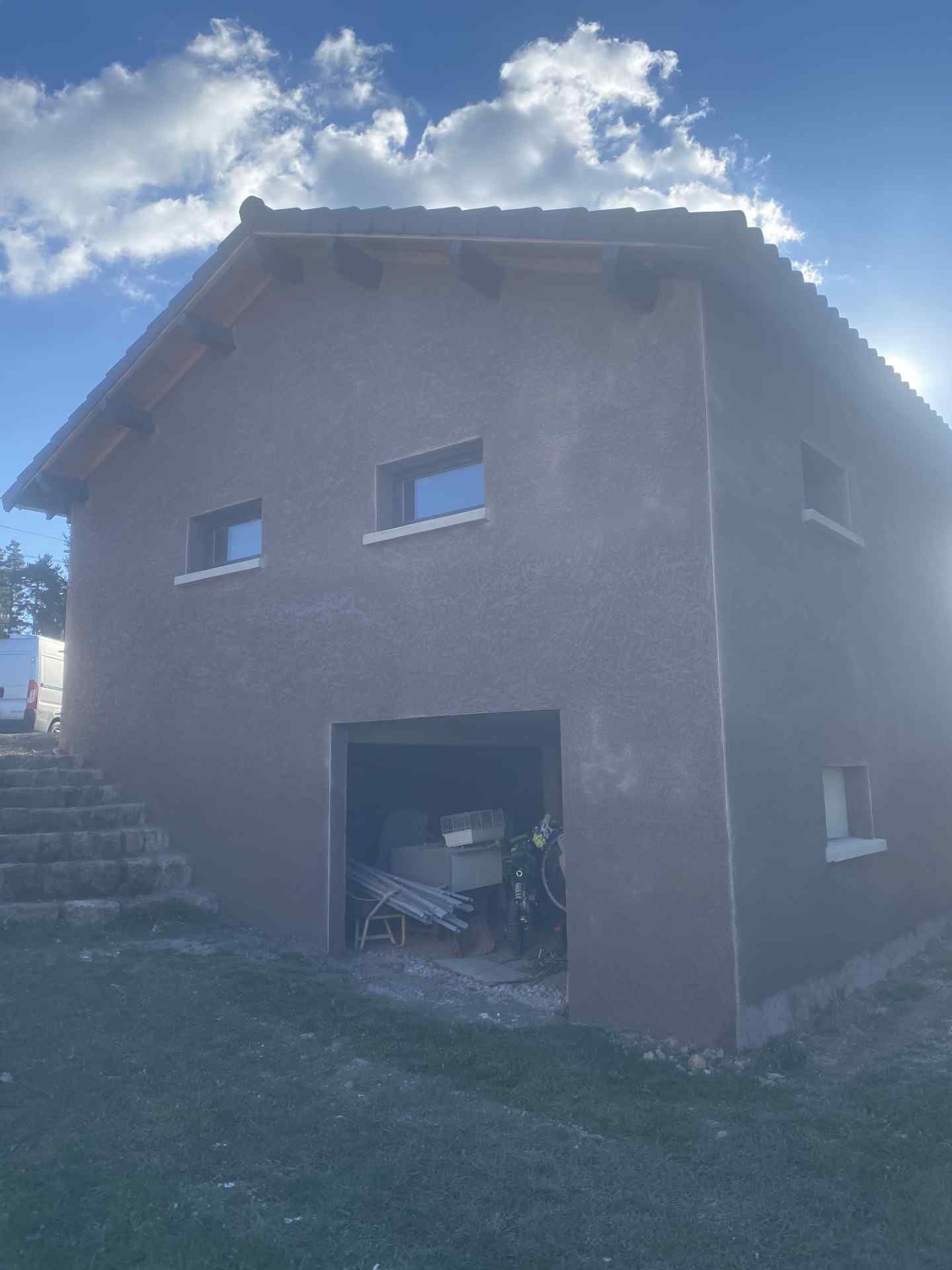 Petite maison en stuc avec garage ouvert, ciel bleu et marches en pierre sur la gauche
