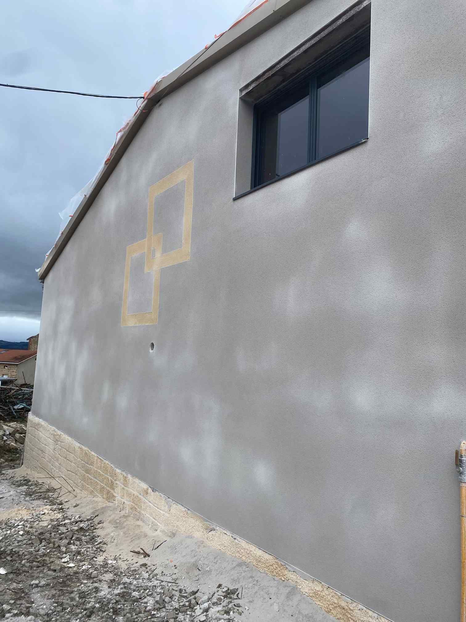 Mur d'un bâtiment gris avec une croix légèrement soulignée de jaune et une fenêtre sombre près de la ligne de toit