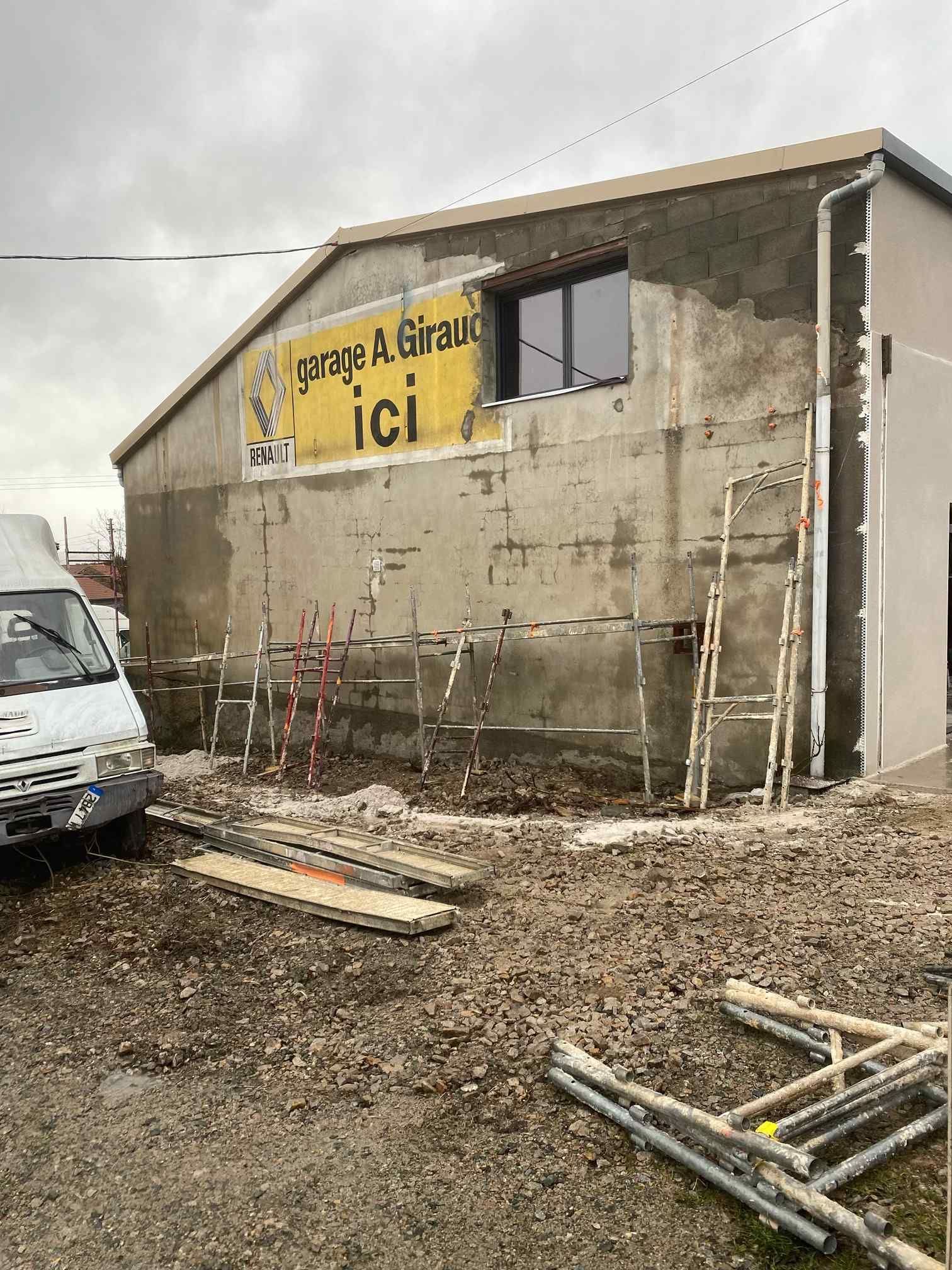 Mur d'un vieux bâtiment avec une enseigne française, échelles et matériaux de construction sur un sol boueux.