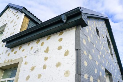 Extérieur de la maison en construction, avec panneaux isolants visibles et garnitures foncées.