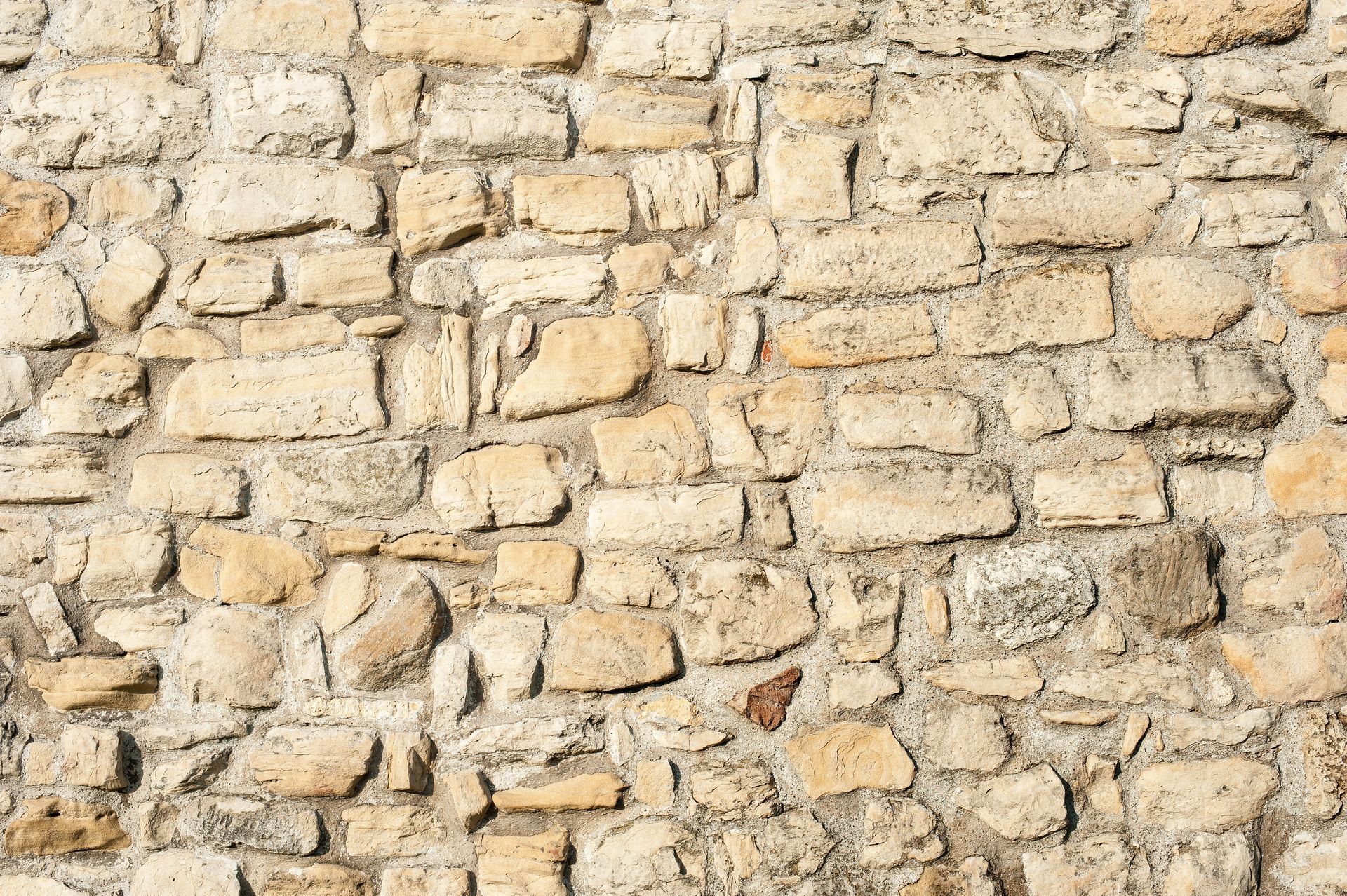 Mur en pierre beige de tailles et de formes variées, texture rugueuse.